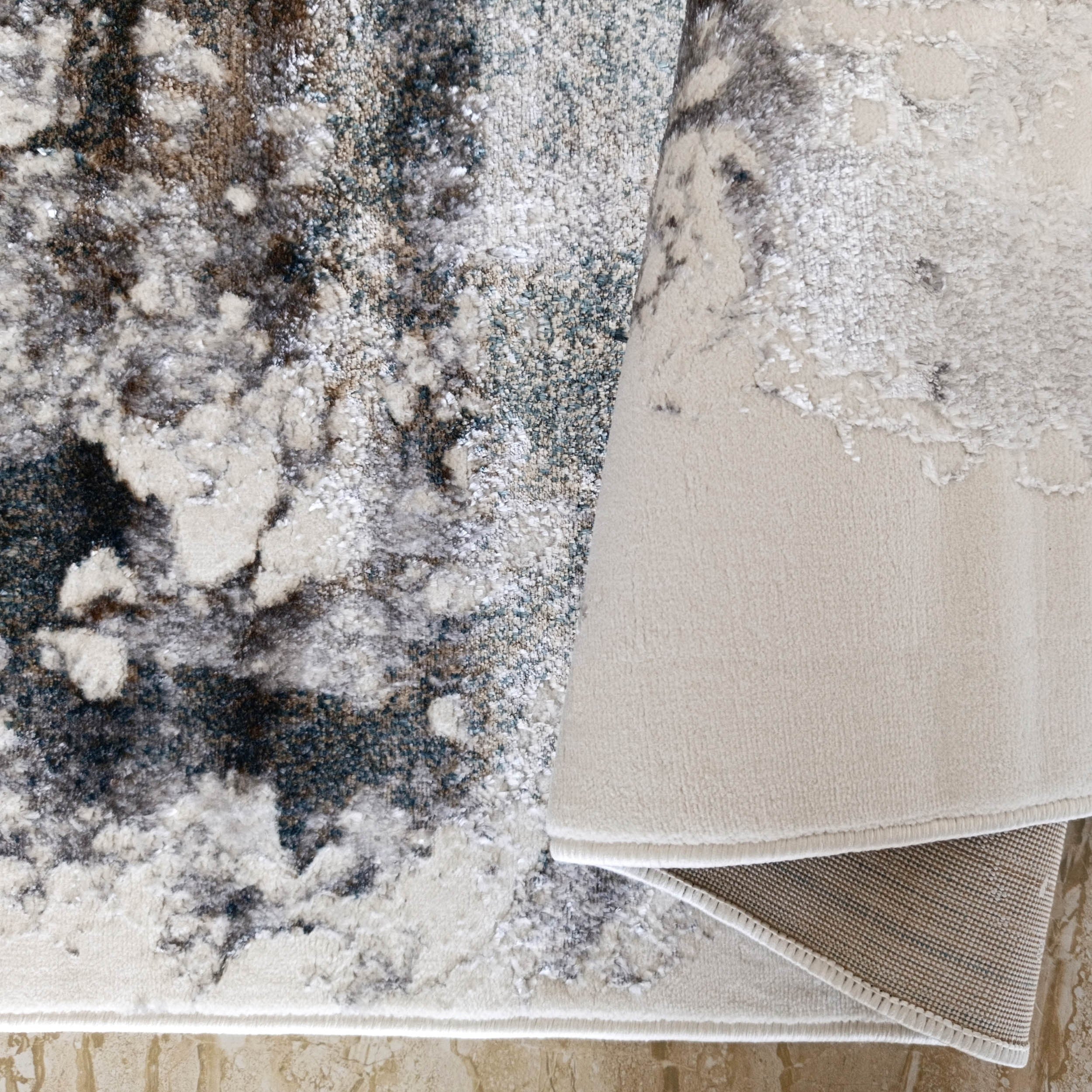 Tapis moelleux aux motifs abstraits crème, gris foncé et marron avec envers tissé beige sous un bord plié sur sol carrelé