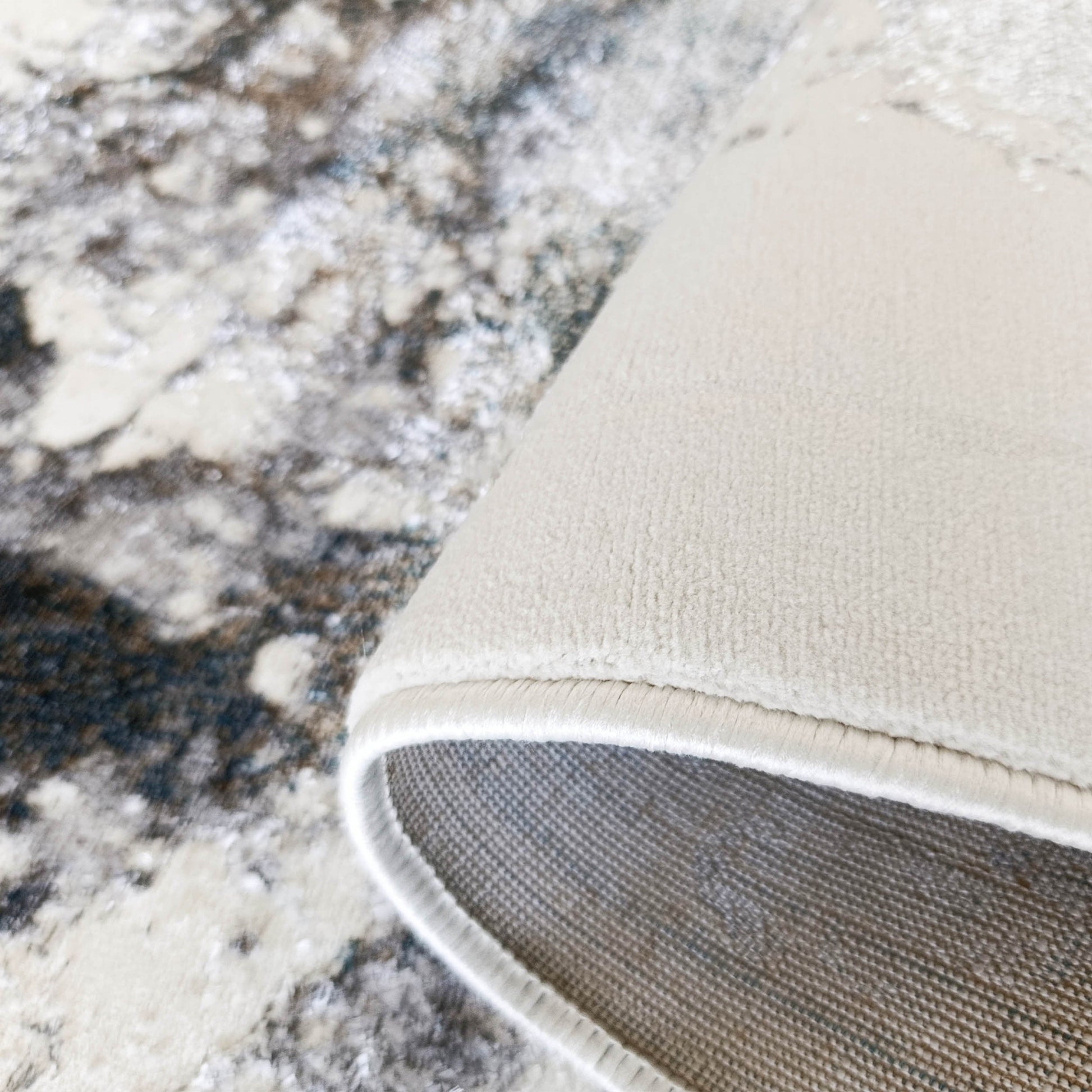 Tapis abstrait marbré crème, beige et gris, bord roulé révélant un envers crème uni et une doublure grise texturée