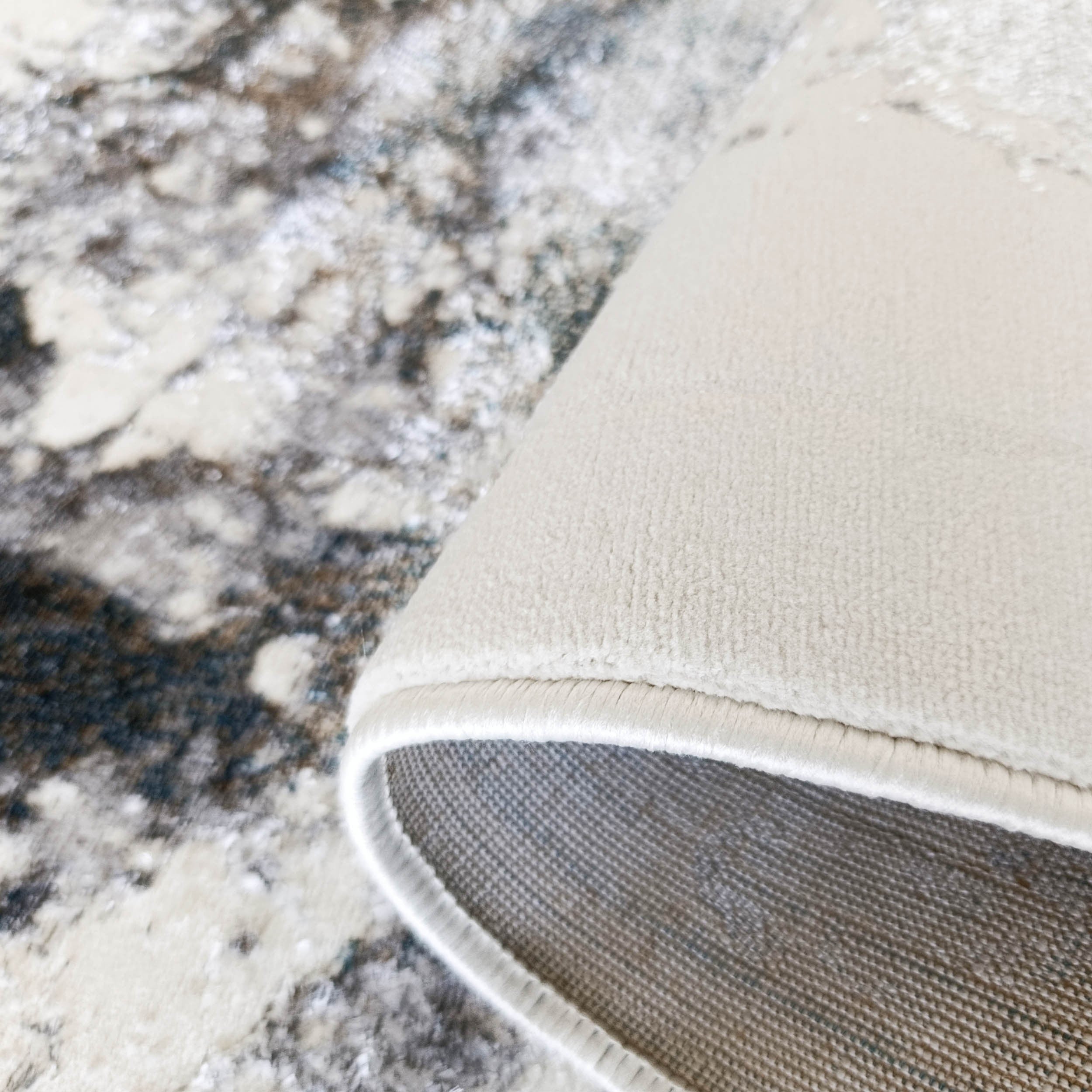 Tapis abstrait marbré crème, beige et gris, bord roulé révélant un envers crème uni et une doublure grise texturée
