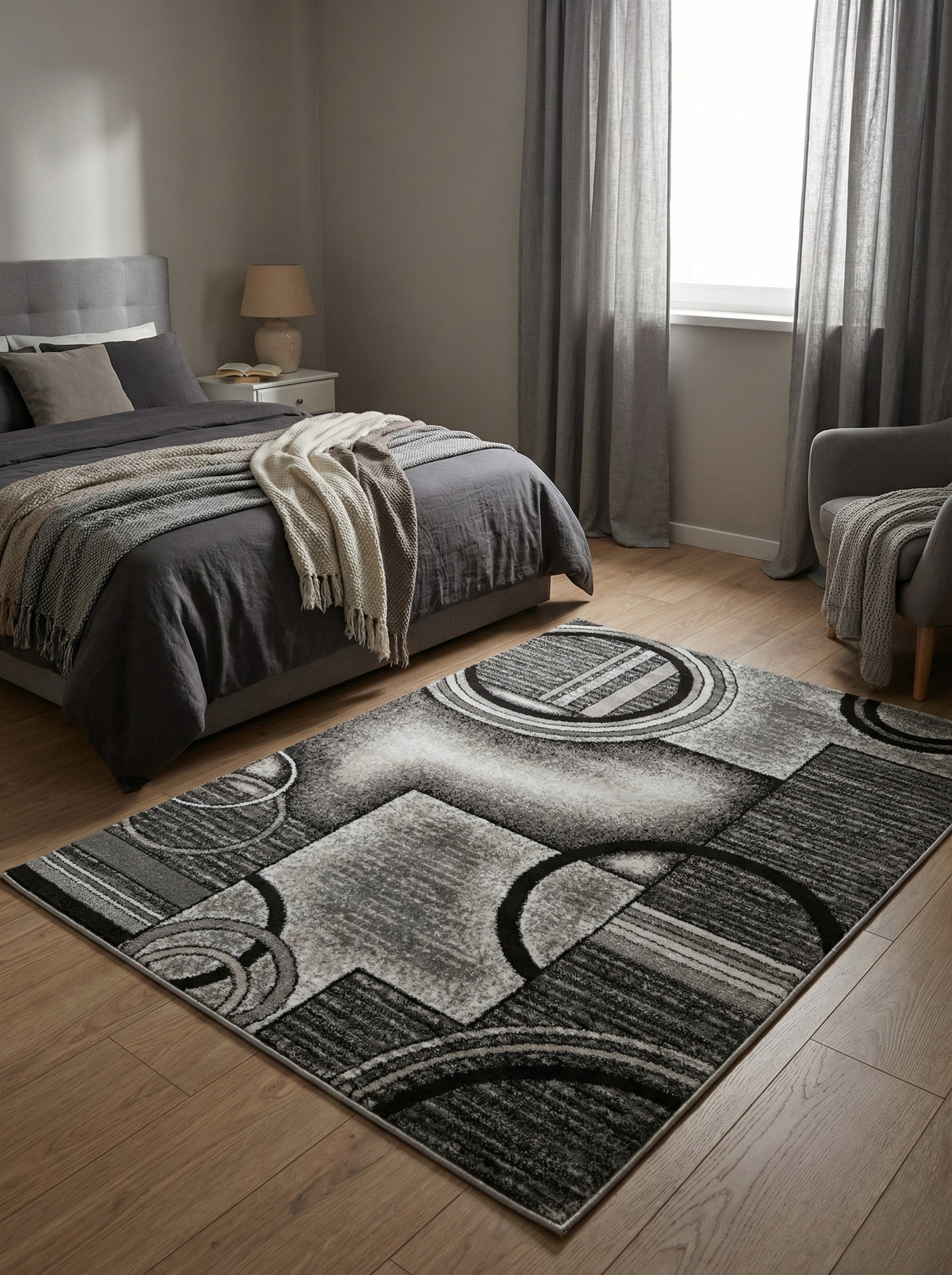 Tapis rectangulaire aux motifs géométriques abstraits gris, noirs et blancs, posé sur un parquet clair dans une chambre moderne