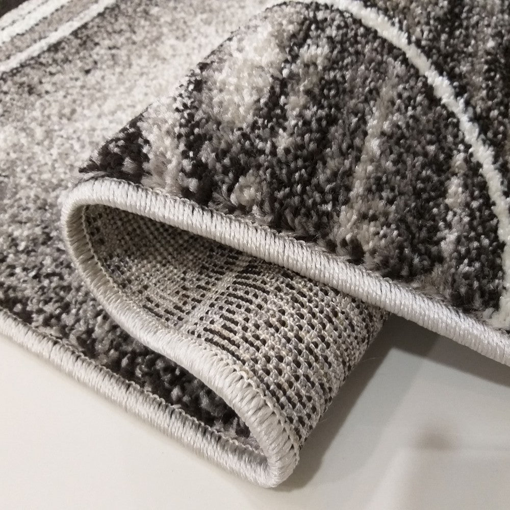 Tapis à poils doux gris, noir et blanc, avec motifs abstraits et lignes, partiellement enroulé, dos tissé visible