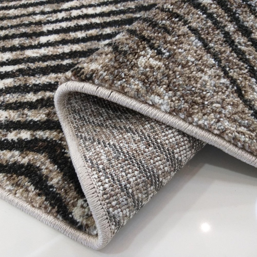 Tapis moelleux à rayures noires, blanches et beiges, envers texturé visible, partiellement enroulé