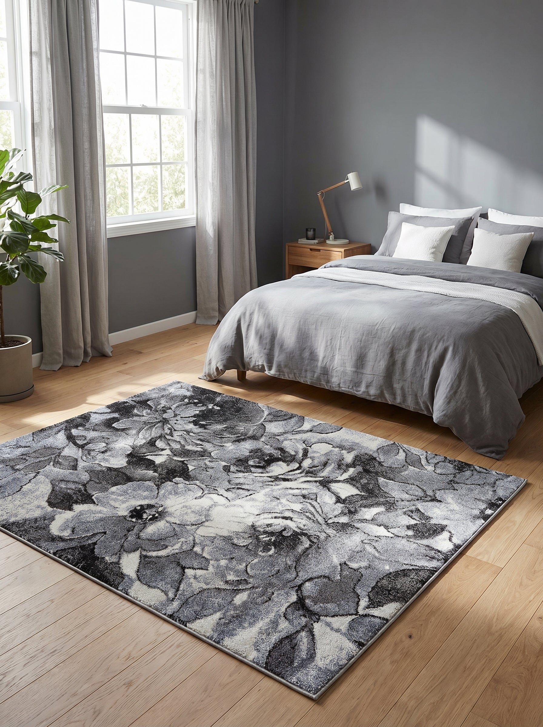 Tapis rectangulaire aux motifs floraux abstraits gris, noirs et blancs, posé sur un parquet clair dans une chambre moderne