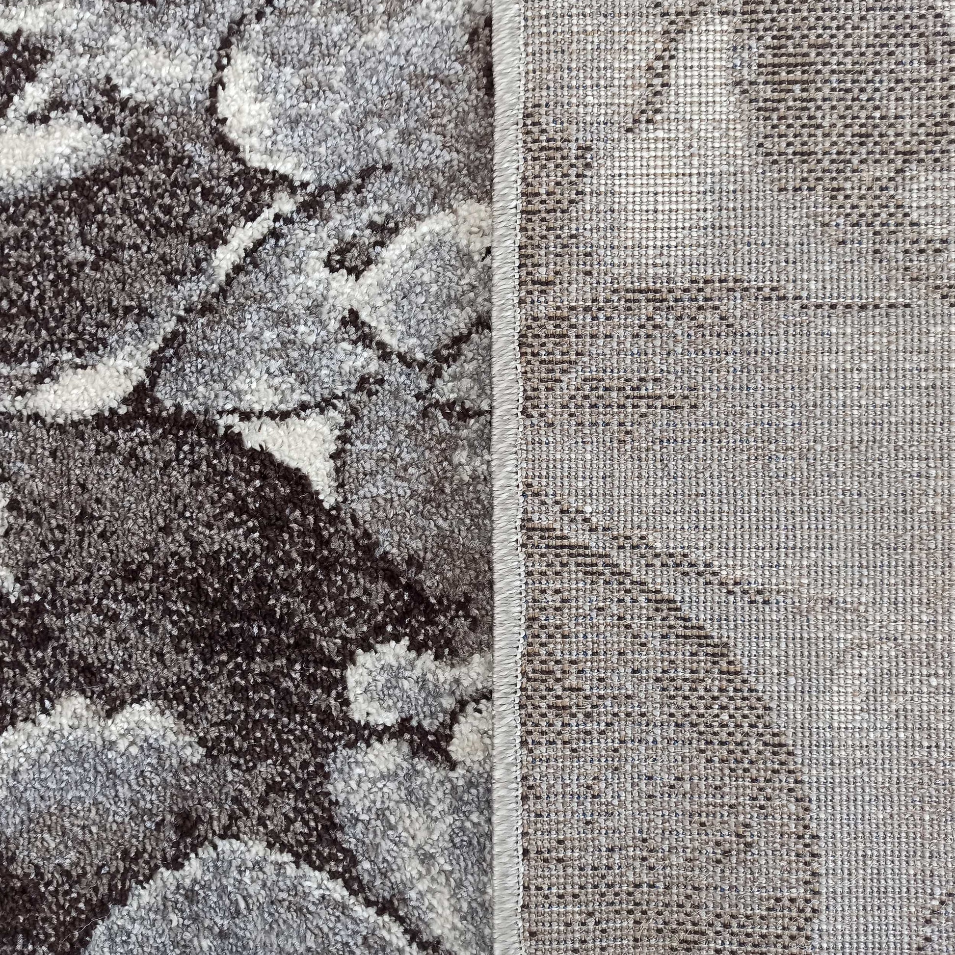 Tapis avec un côté au velours épais à motifs gris, blancs et marron, et l'autre côté montrant son envers tissé