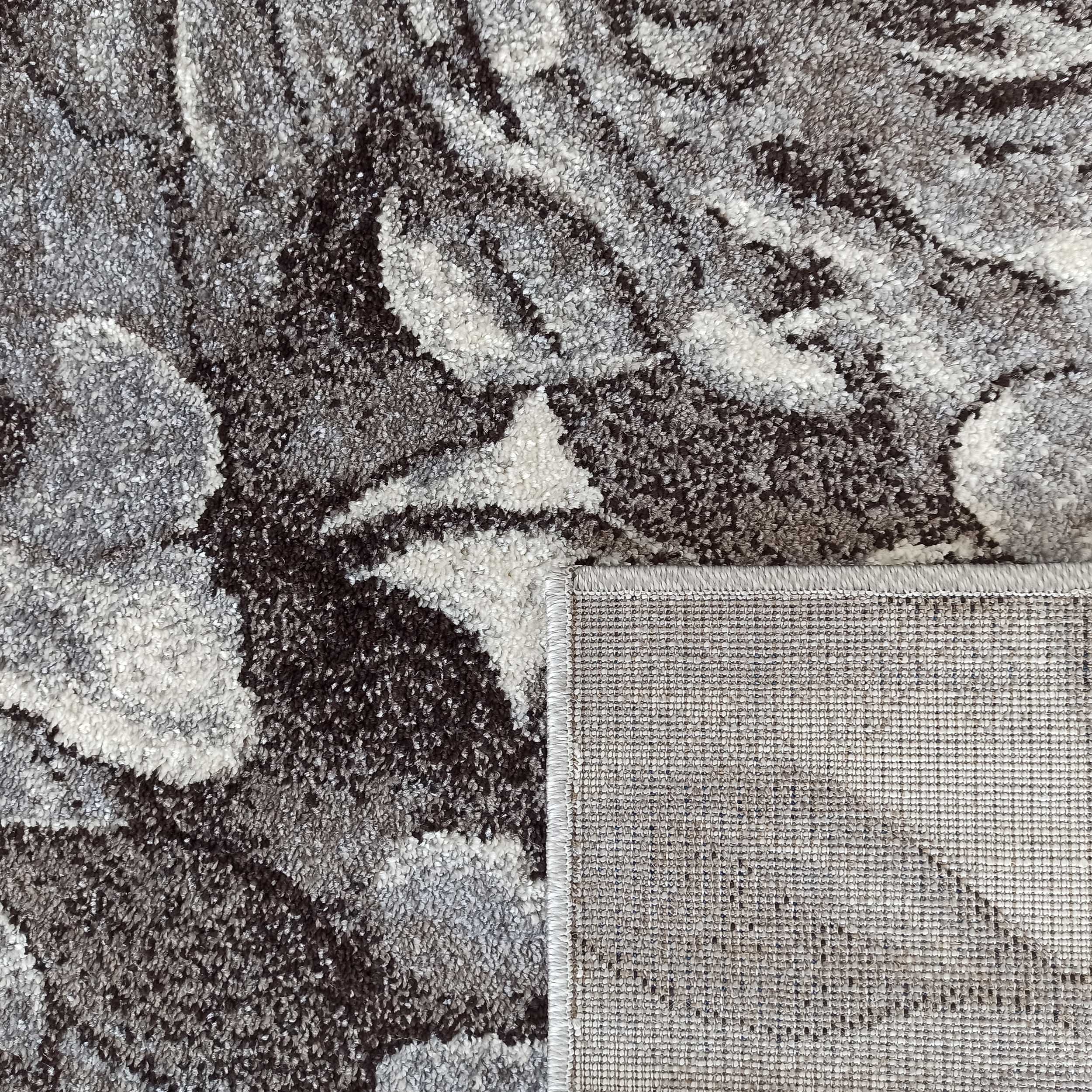 Tapis texturé aux motifs abstraits gris clairs et foncés, avec son envers quadrillé et son bord surpiqué apparent