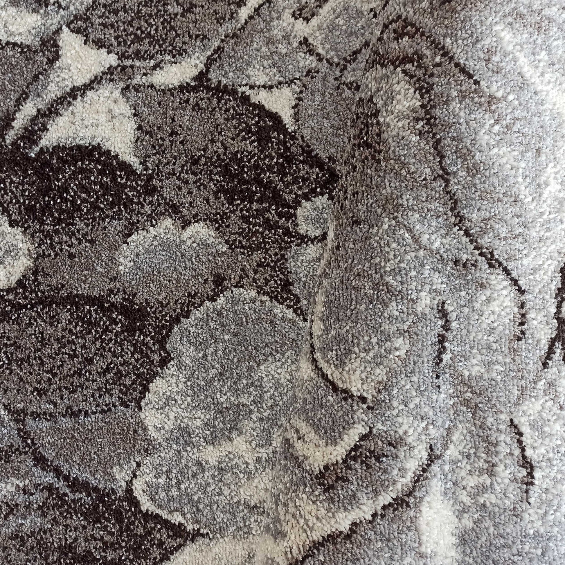 Tapis moelleux à motifs abstraits gris clair, gris moyen et très foncé, avec une surface texturée et une zone repliée