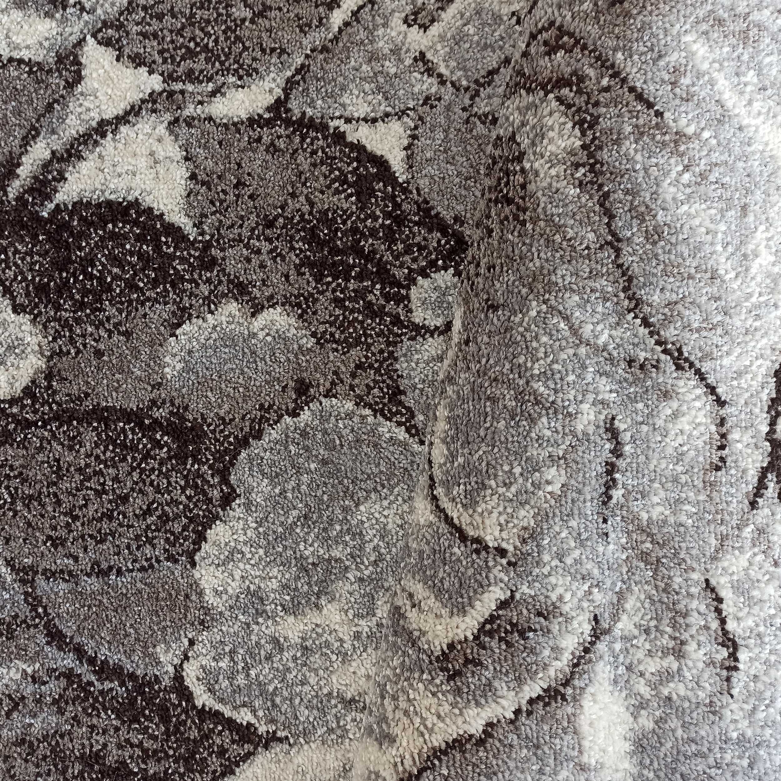 Tapis moelleux à motifs abstraits gris clair, gris moyen et très foncé, avec une surface texturée et une zone repliée
