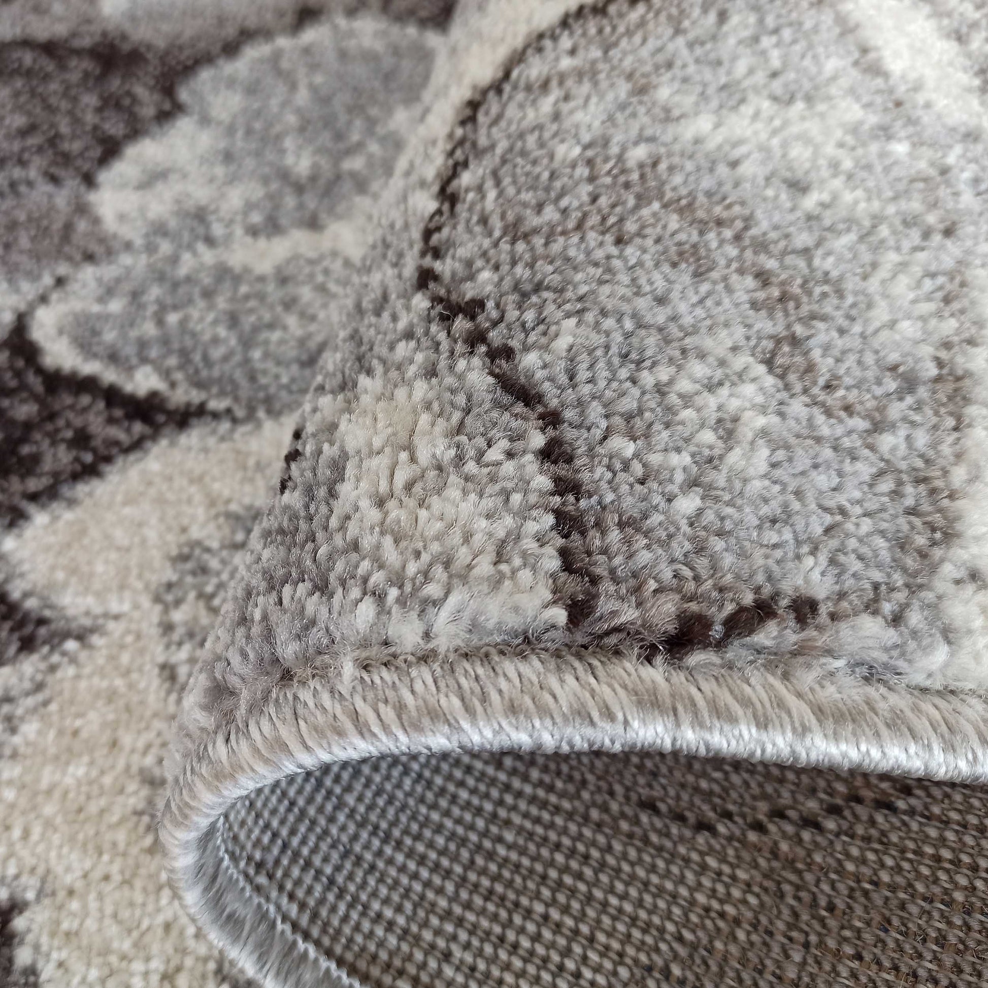 Tapis texturé, roulé sur un côté, avec des motifs abstraits gris clair, gris foncé et marron. Le velours du tapis est doux et le dos est tissé