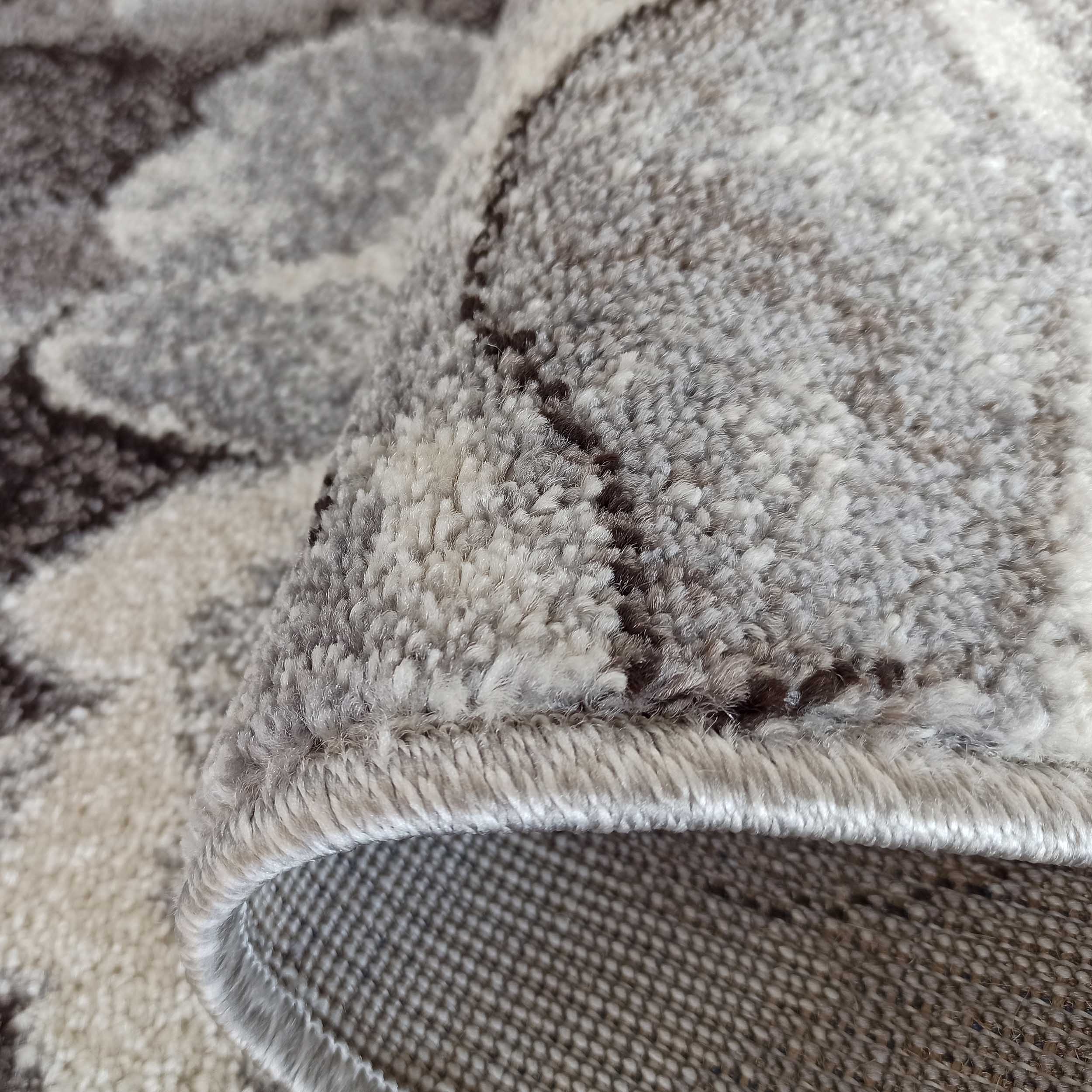 Tapis texturé, roulé sur un côté, avec des motifs abstraits gris clair, gris foncé et marron. Le velours du tapis est doux et le dos est tissé