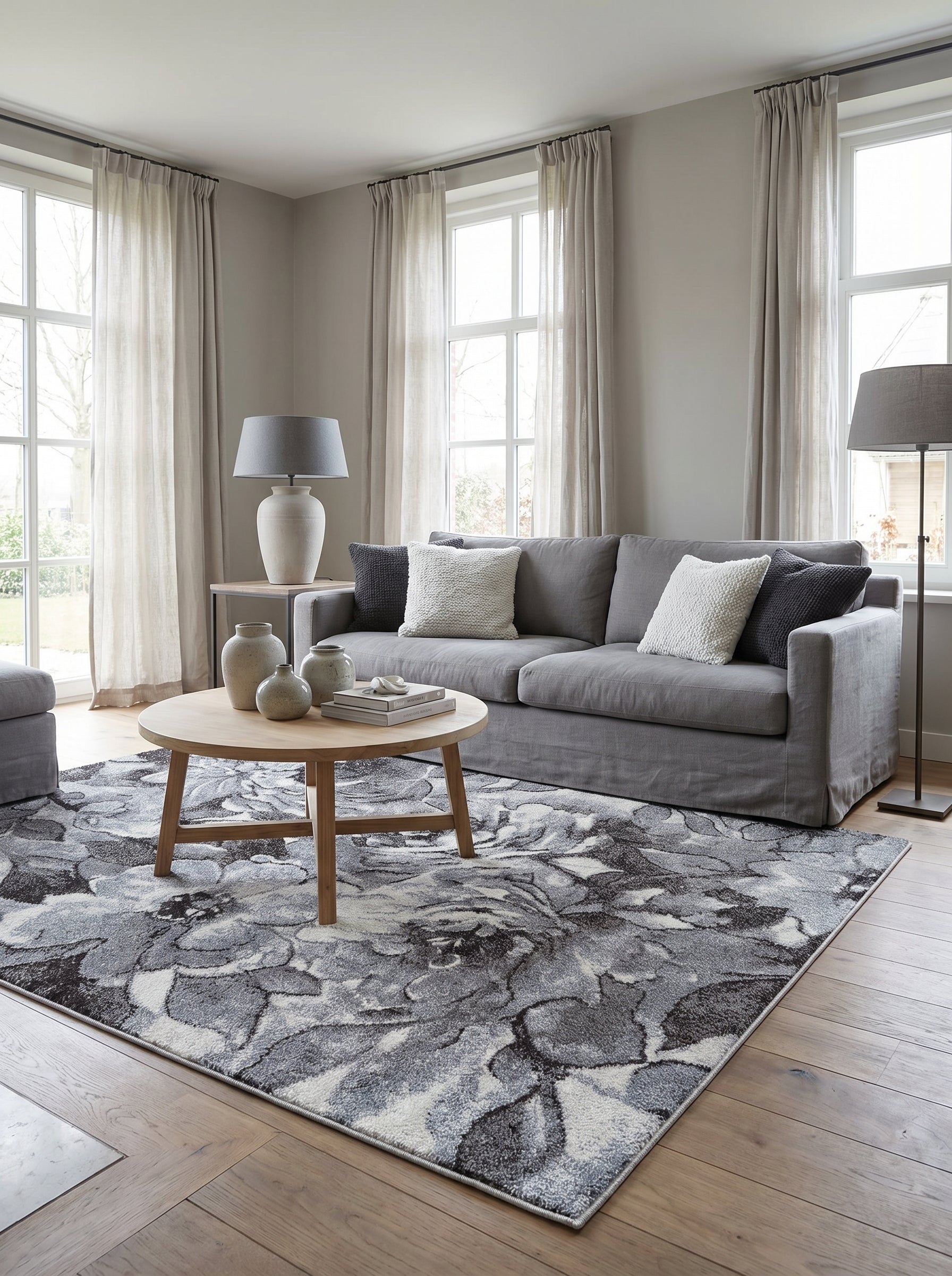Tapis rectangulaire en matière textile, orné de larges motifs floraux abstraits gris, blancs et noirs, dans un salon lumineux