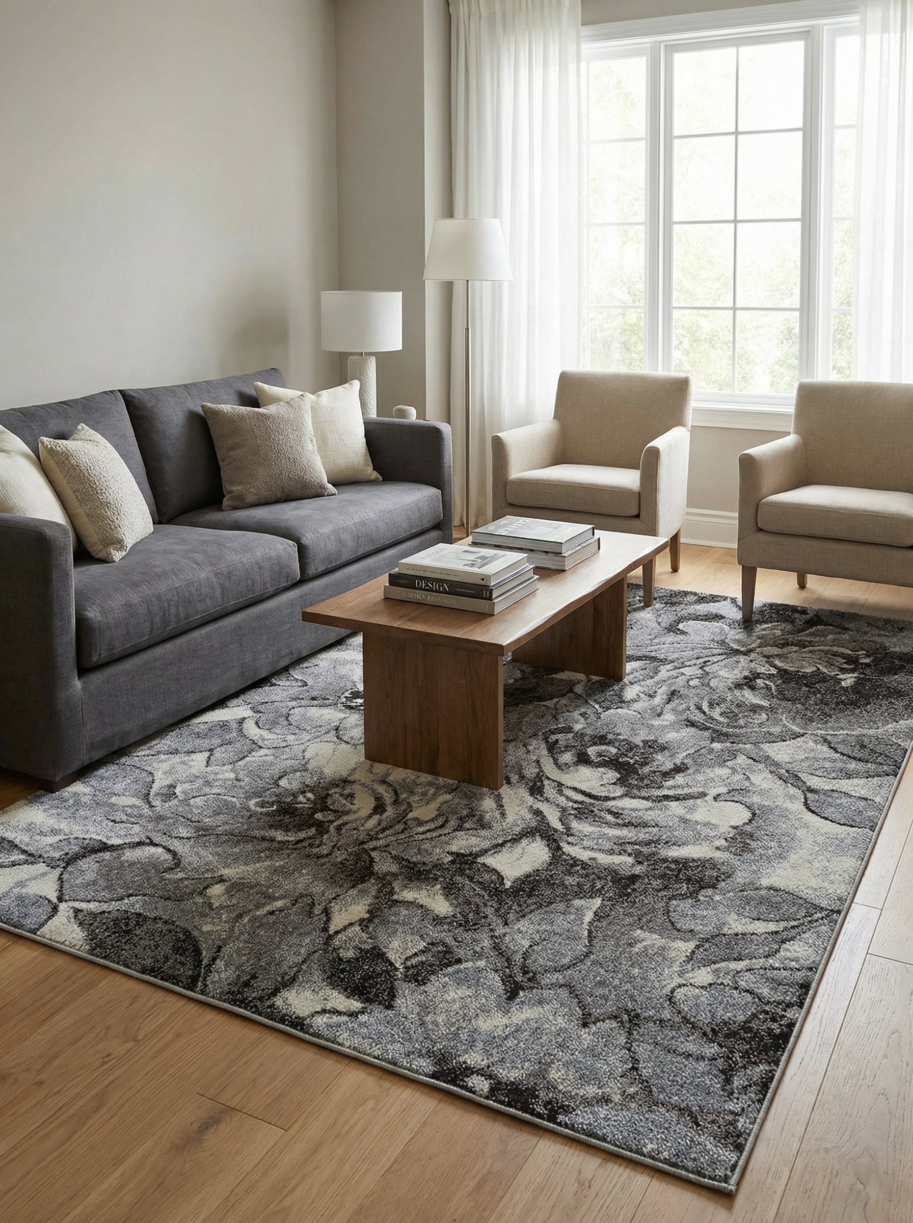 Tapis rectangulaire aux motifs floraux abstraits gris foncé, gris clair et blanc cassé, posé sur un parquet dans un salon