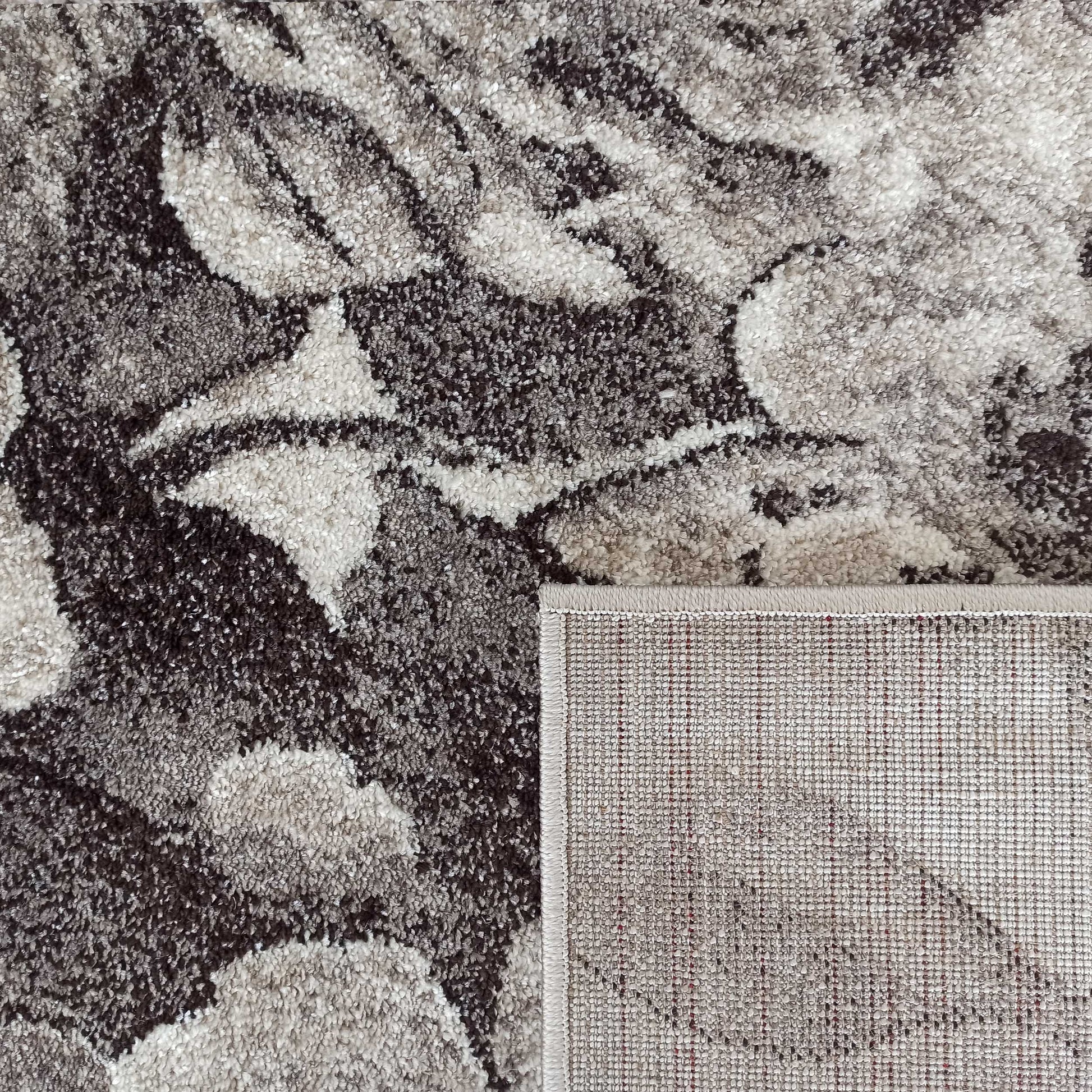 Tapis moelleux aux motifs abstraits gris, marron, beige et blanc cassé, avec un coin replié montrant le revers tissé