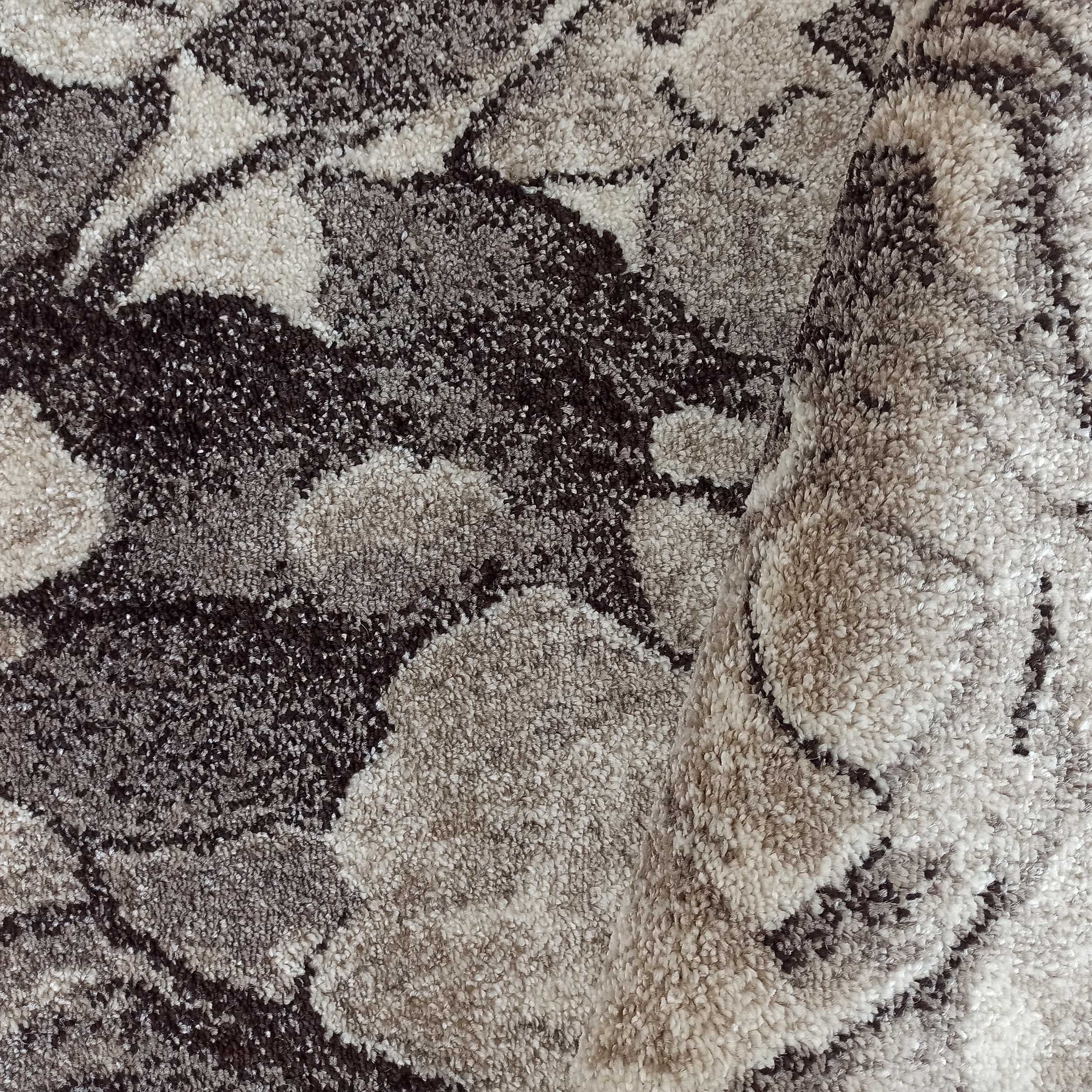 Tapis moelleux aux motifs abstraits dans des tons de gris, marron et beige, légèrement roulé