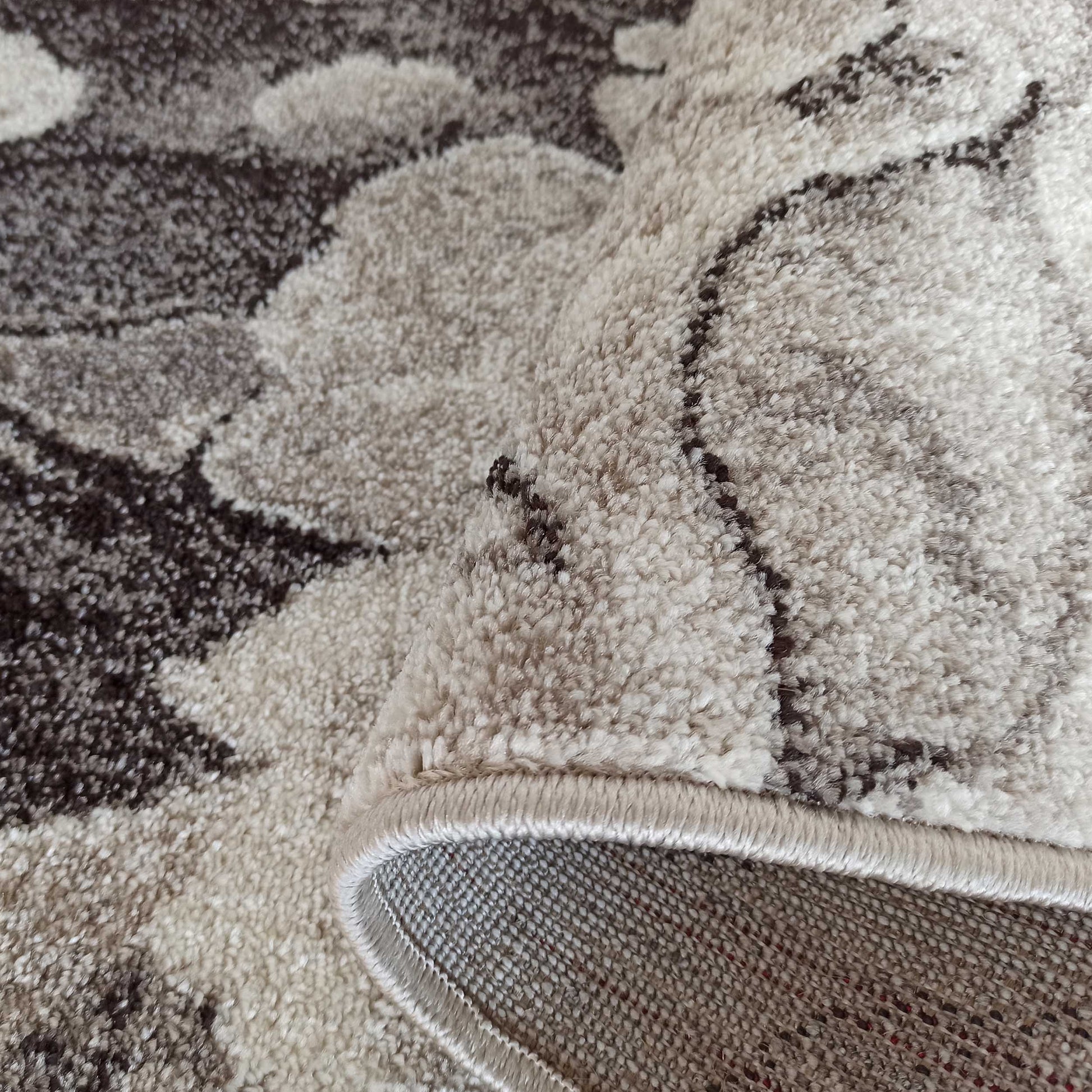 Tapis à la texture bouclée, avec des motifs floraux abstraits en camaïeu de marron et beige, partiellement enroulé