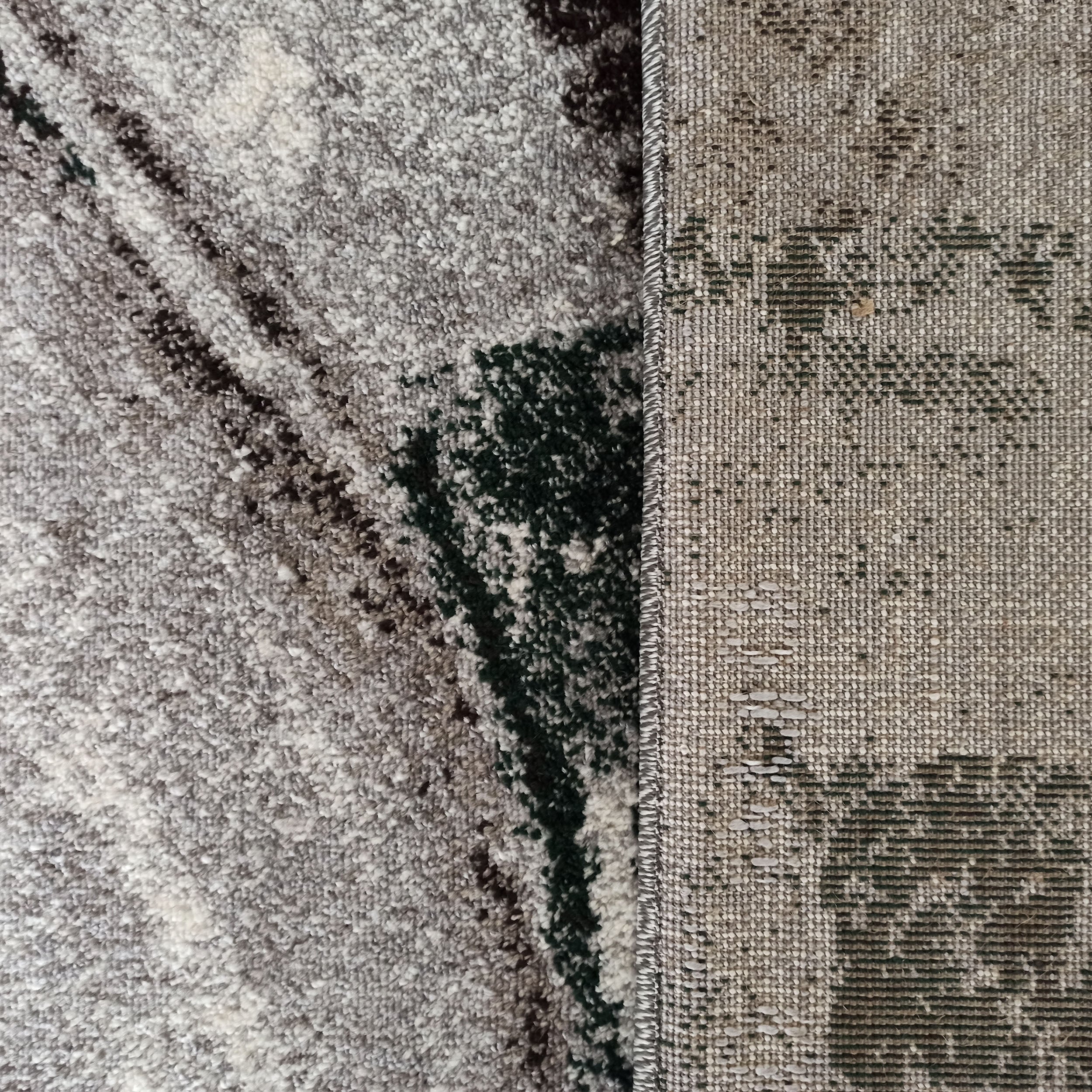 Tapis texturé gris, blanc, noir et vert foncé à motifs abstraits, avec sa face inférieure tissée beige à motifs sombres