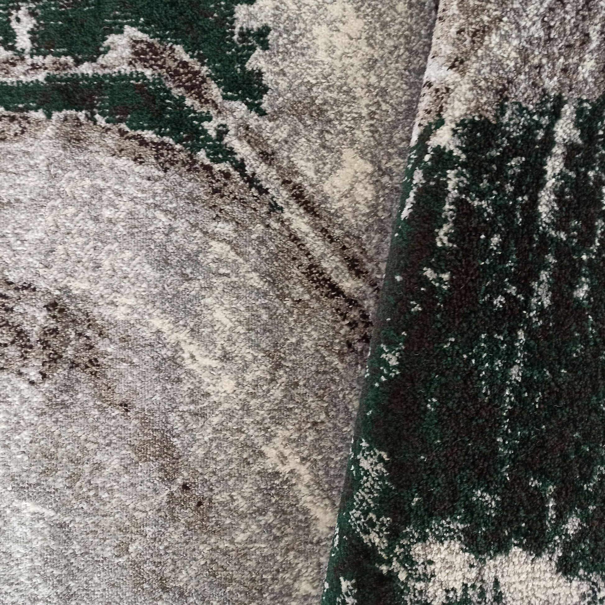 Tapis à poils doux avec des motifs abstraits et des nuances de vert forêt, gris et brun, plié
