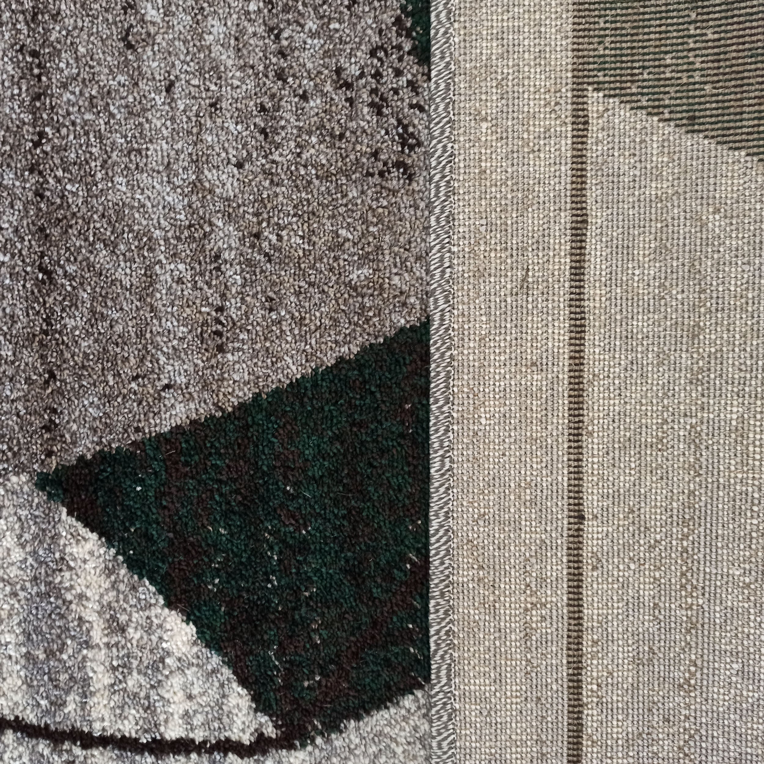 Tapis texturé gris, marron et vert foncé aux motifs géométriques, son revers tissé beige et gris est apparent