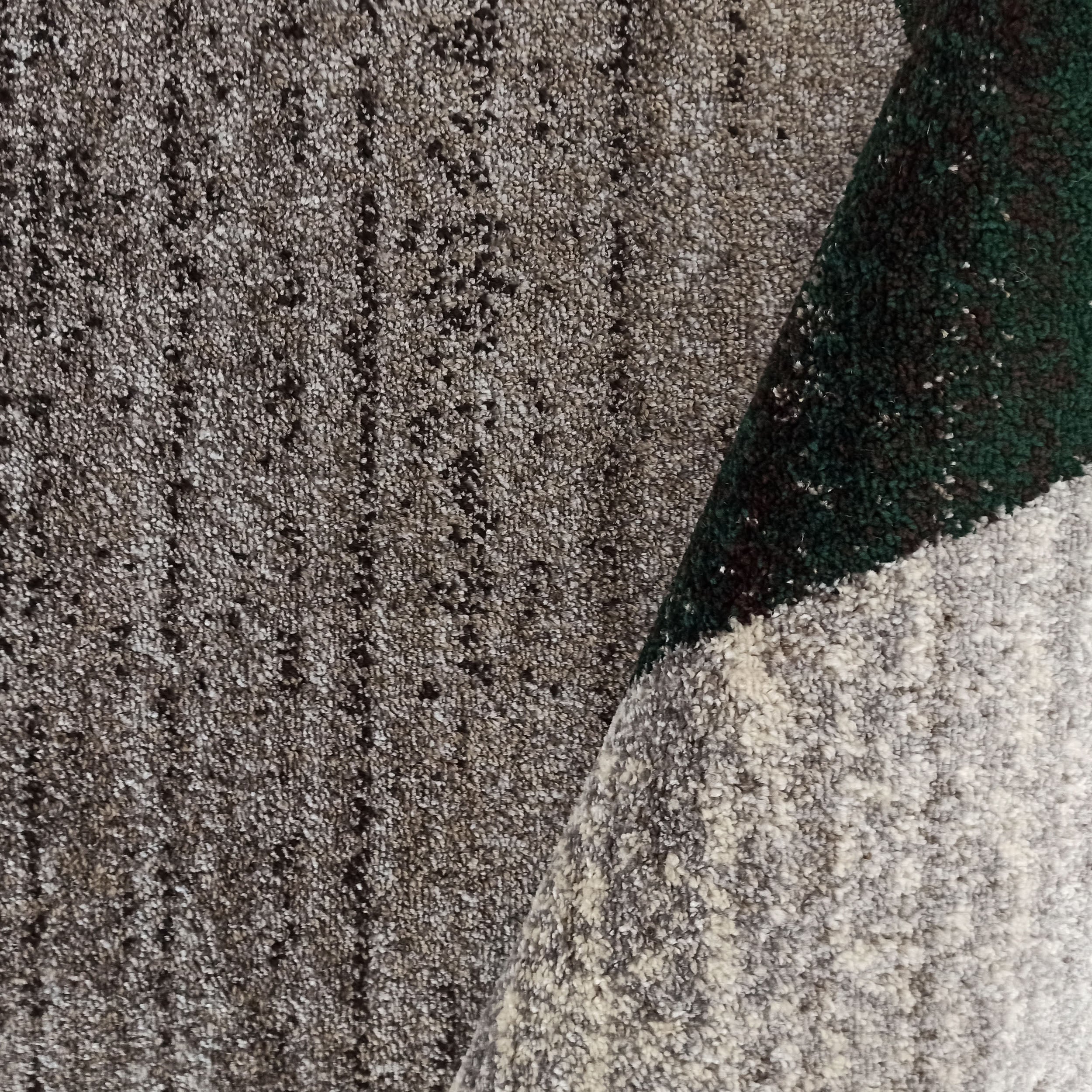 Tapis à poils bouclés gris, marron et crème avec subtiles rayures, un pli révèle une section vert sombre et une autre gris clair