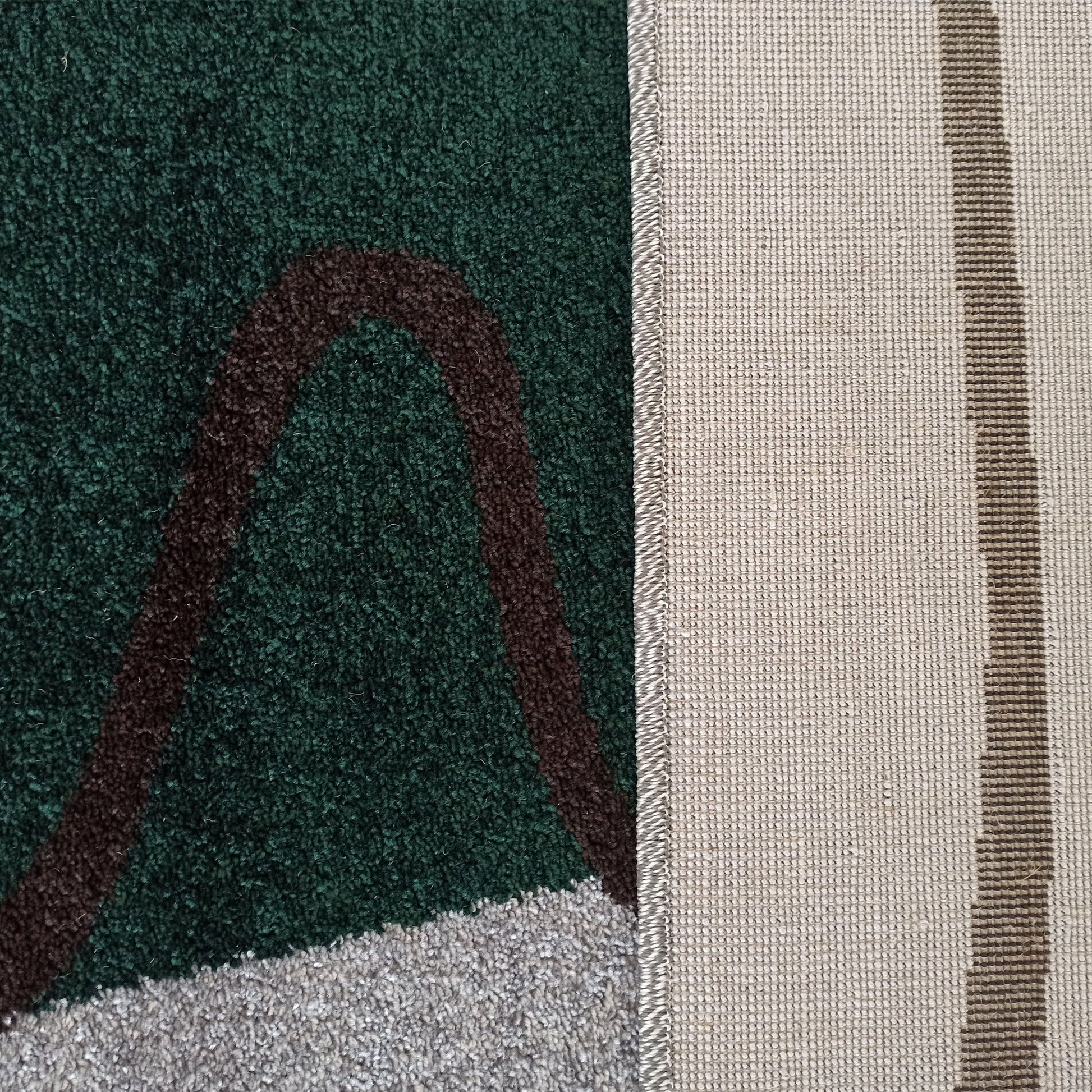 Tapis avec une surface à poils longs verte, marron et grise, et un dessous tissé beige à bande marron