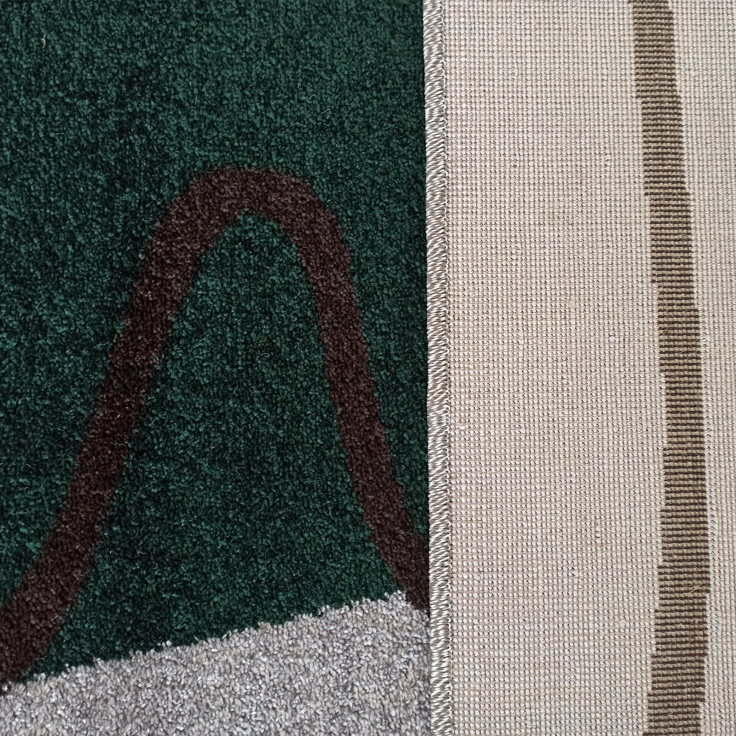Tapis avec une surface à poils longs verte, marron et grise, et un dessous tissé beige à bande marron