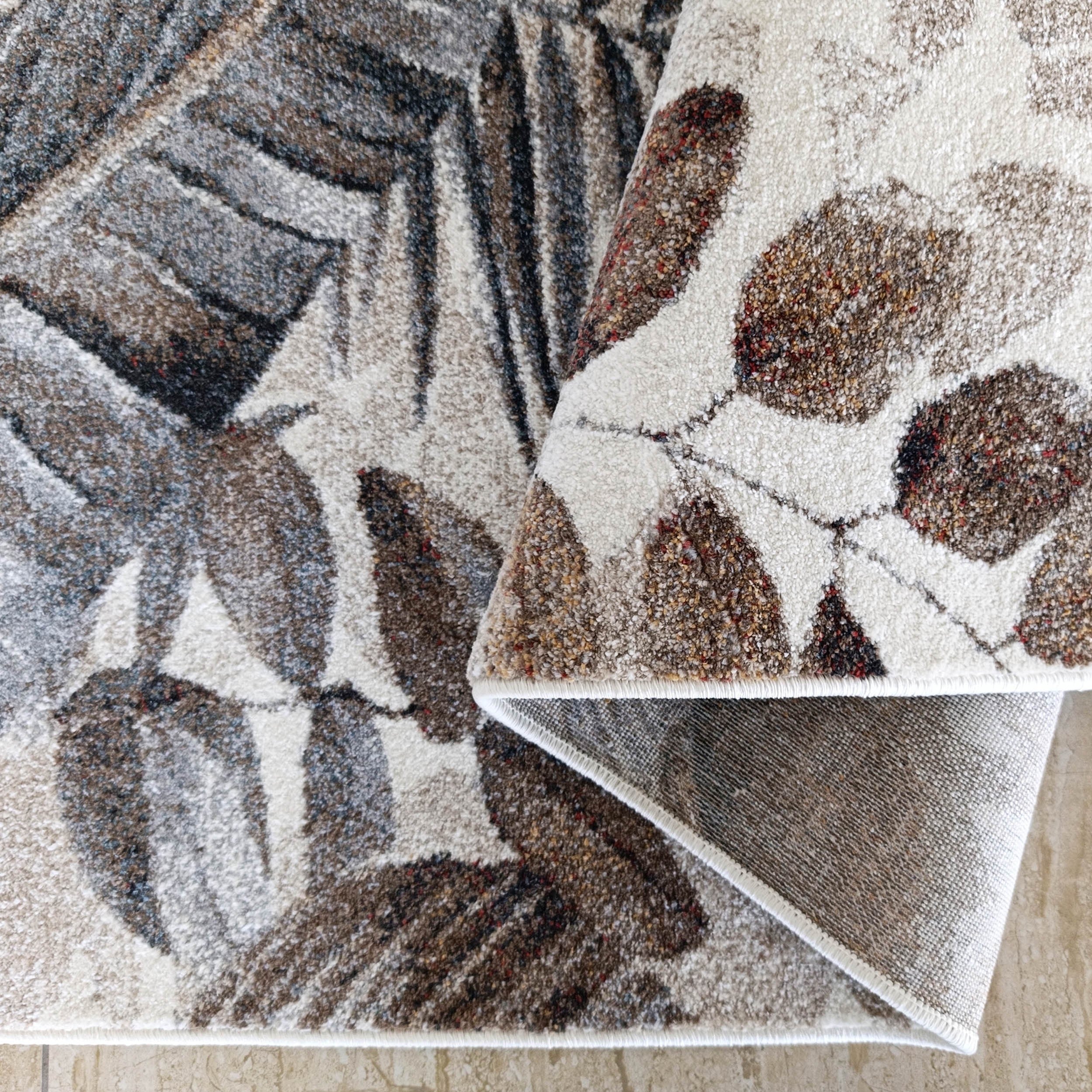 Tapis à poils ras beige, brun et gris aux motifs de feuilles stylisées, partiellement roulé sur un sol carrelé clair