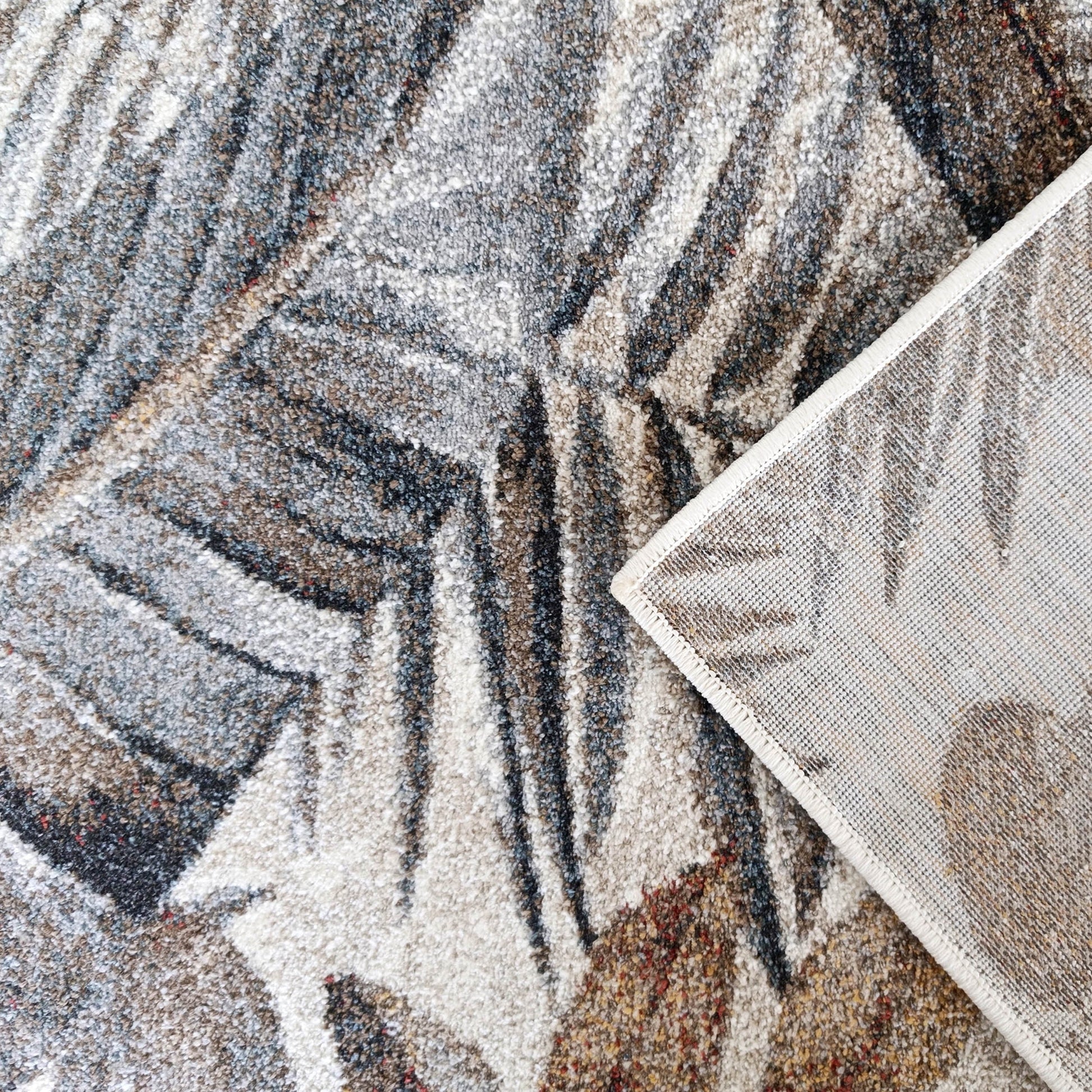 Tapis texturé à motifs de feuillage gris, beige, marron, bleu et rouge révélant un revers tissé crème