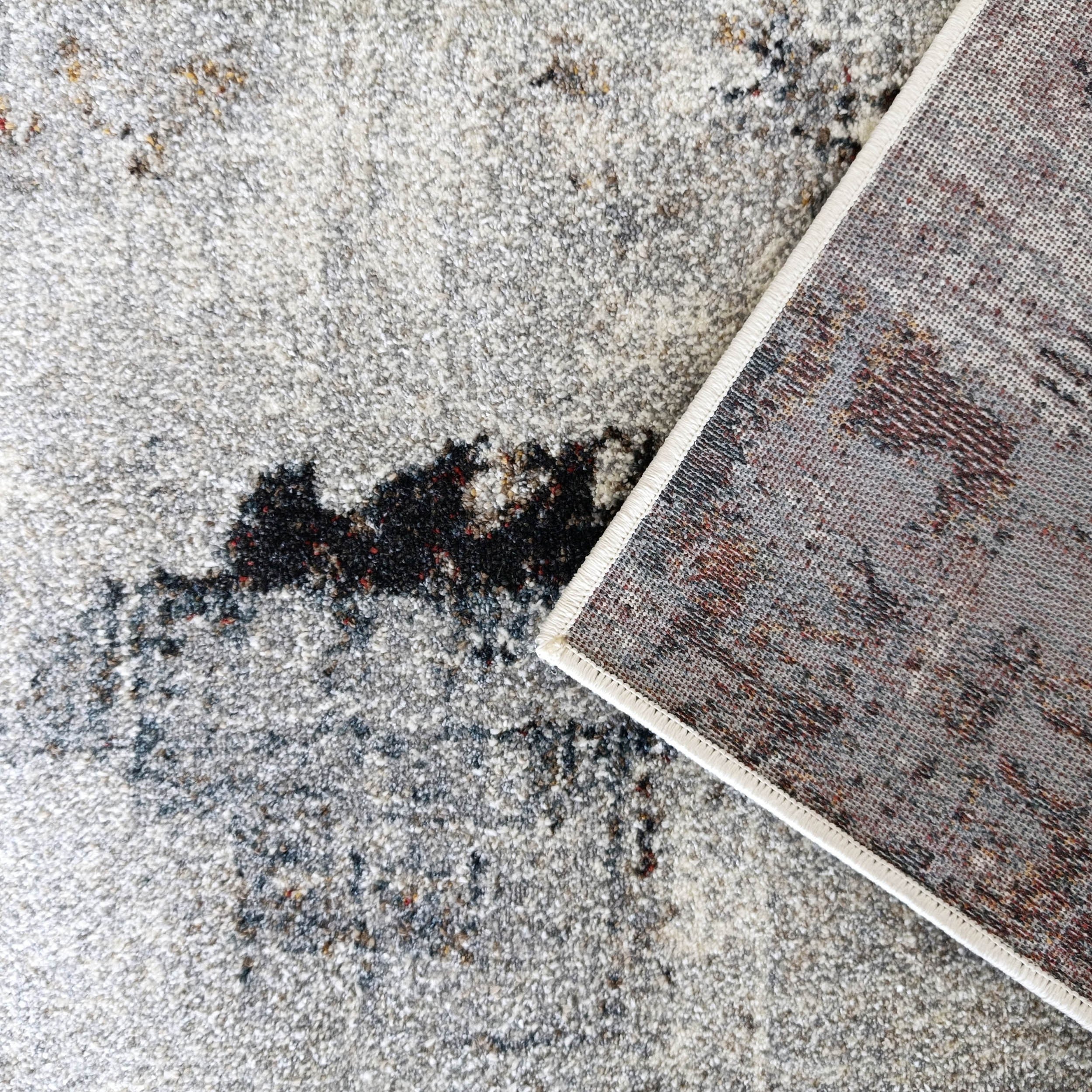 Tapis tissé texturé gris clair et blanc, motifs abstraits foncés et rouges, bordure blanche cousue