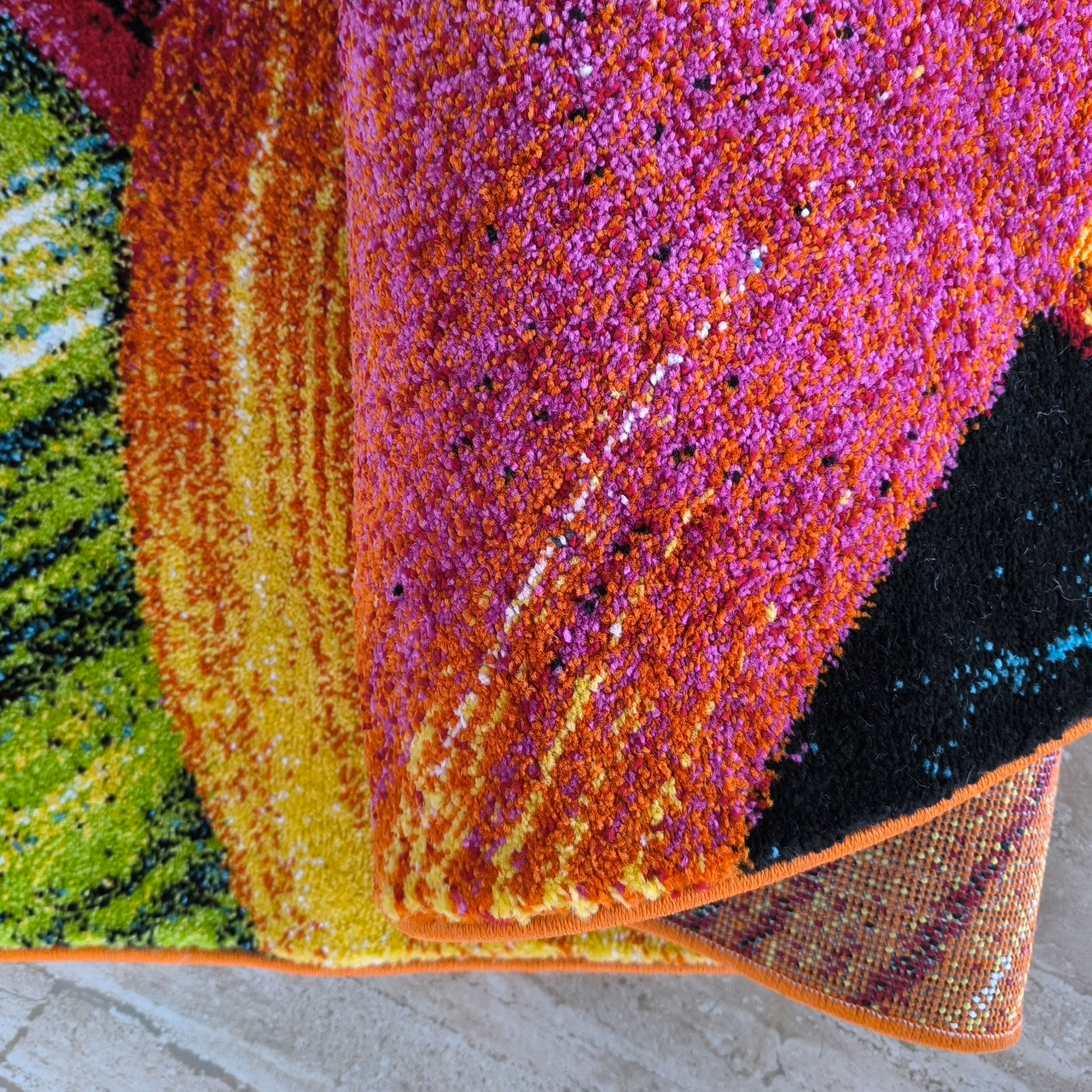 Tapis aux fibres épaisses et au design abstrait éclatant, mêlant des teintes de rose, orange, jaune, vert et noir