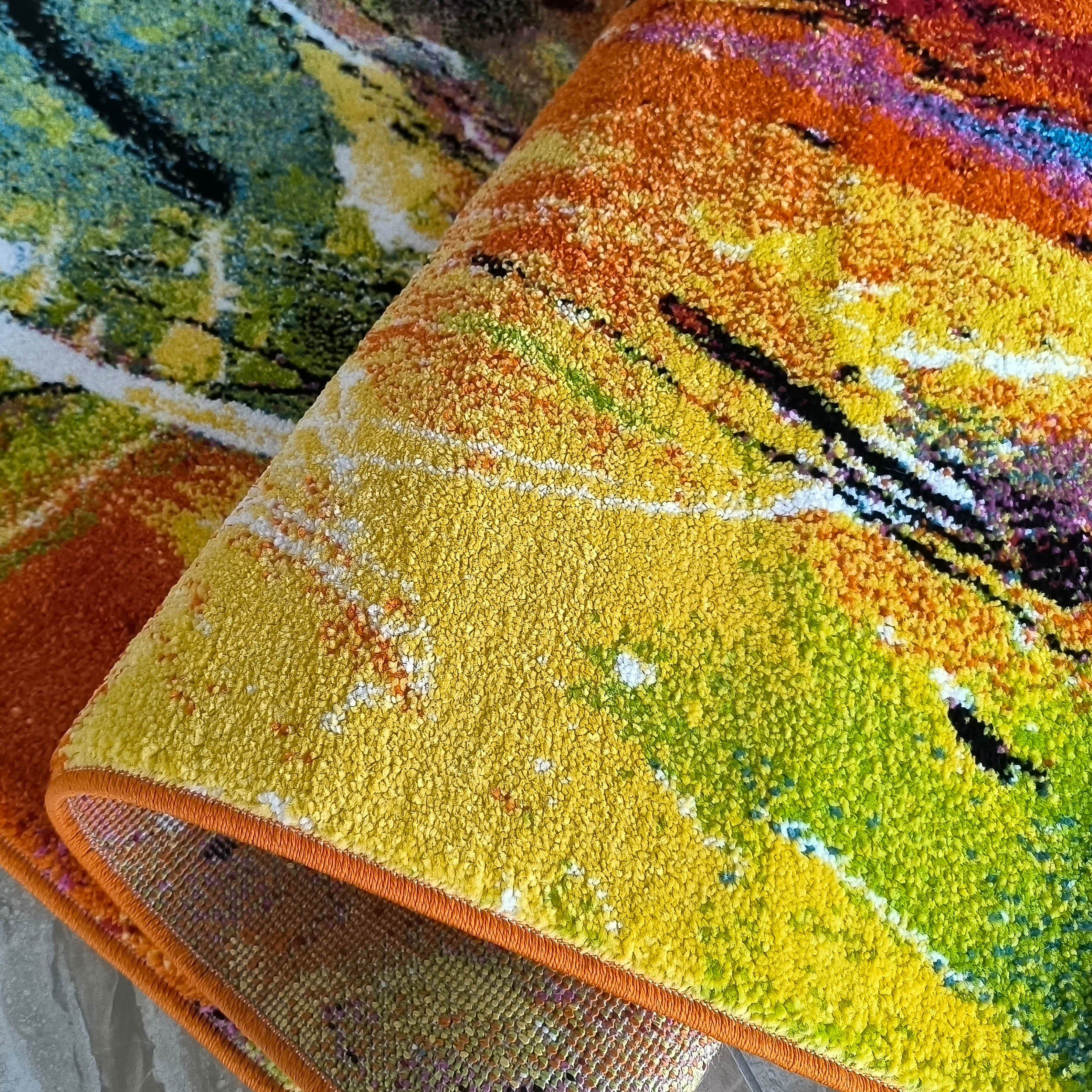 Tapis aux motifs abstraits d'éclaboussures en jaune, orange, vert, bleu, rouge et noir, avec une surface texturée et une bordure orange