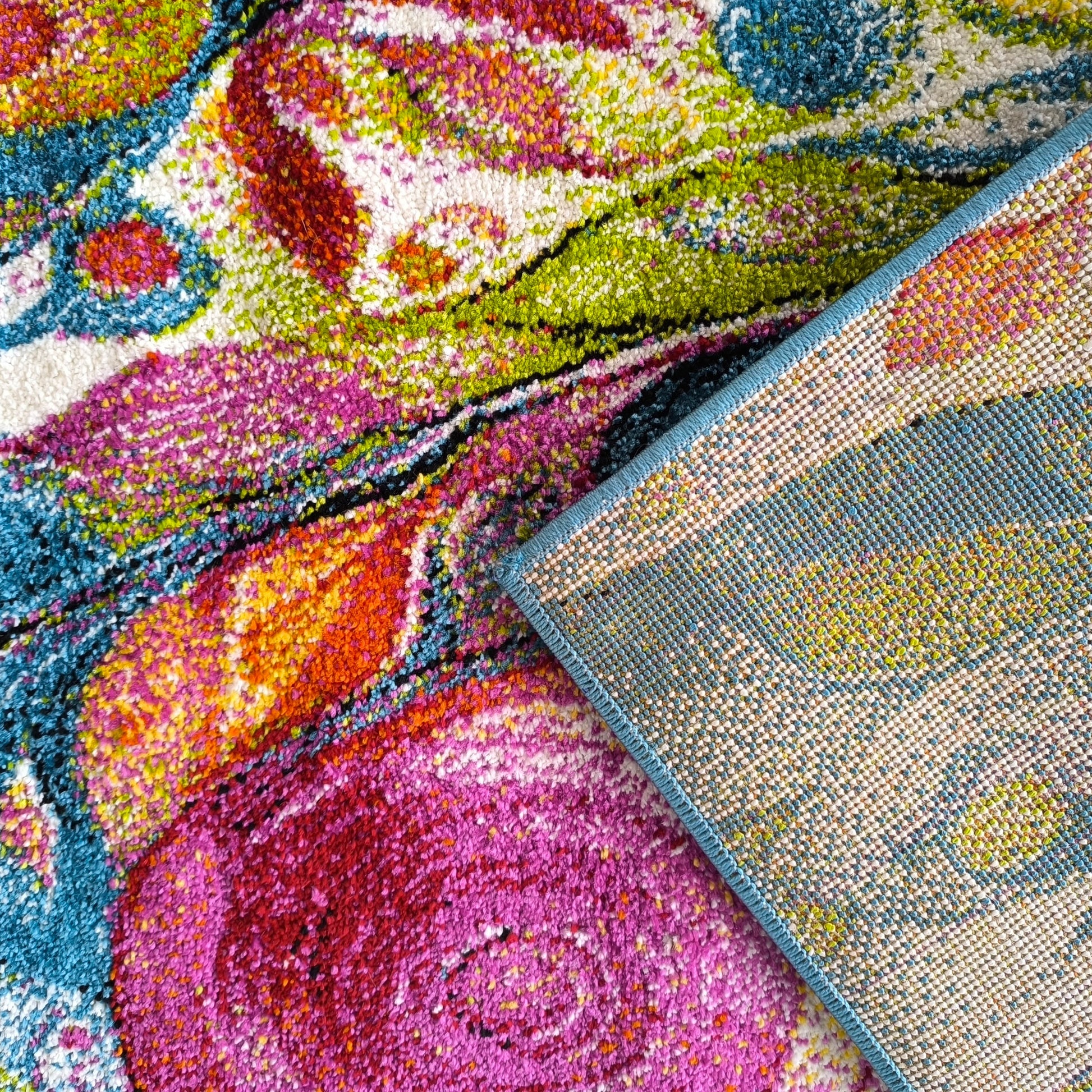 Tapis à poils longs aux couleurs vives fuchsia, vert, bleu et orange avec des motifs abstraits. Le coin plié révèle le dessous tissé