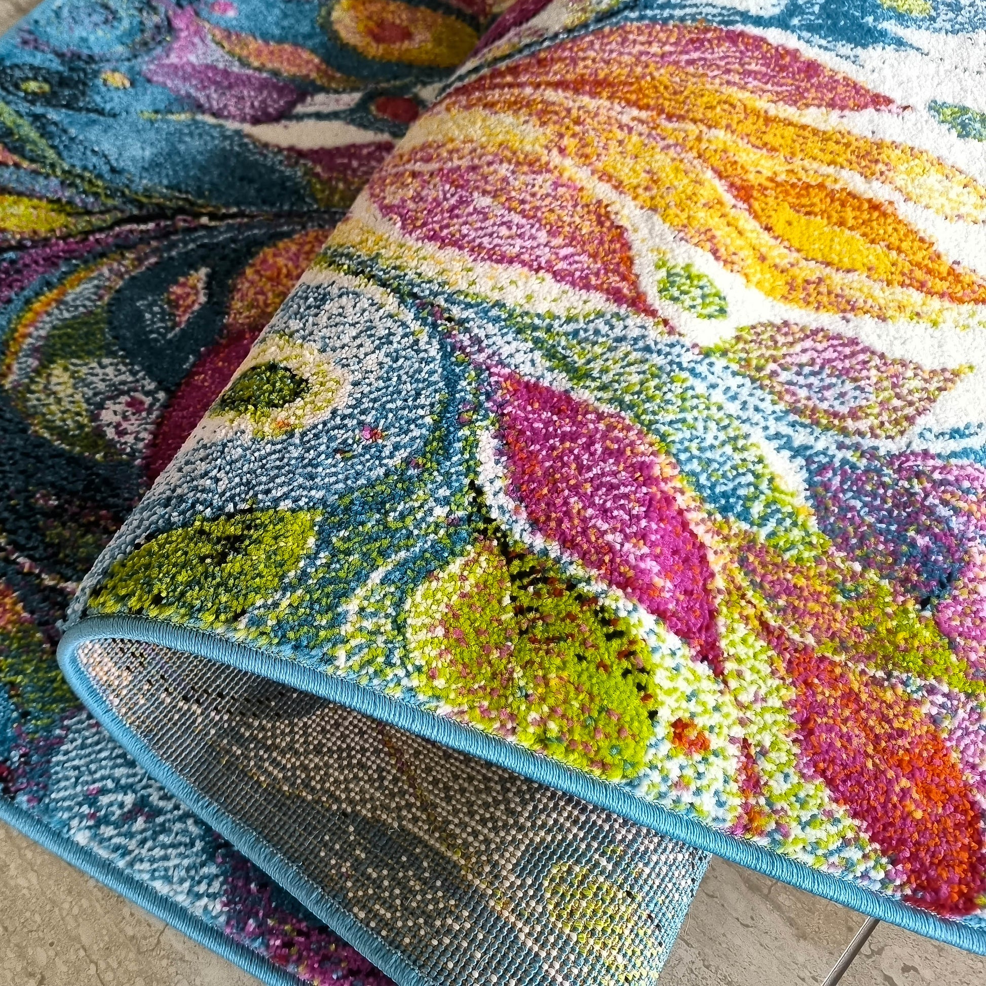 Tapis multicolore, motifs abstraits et poils doux. Partiellement roulé, il révèle son envers tissé