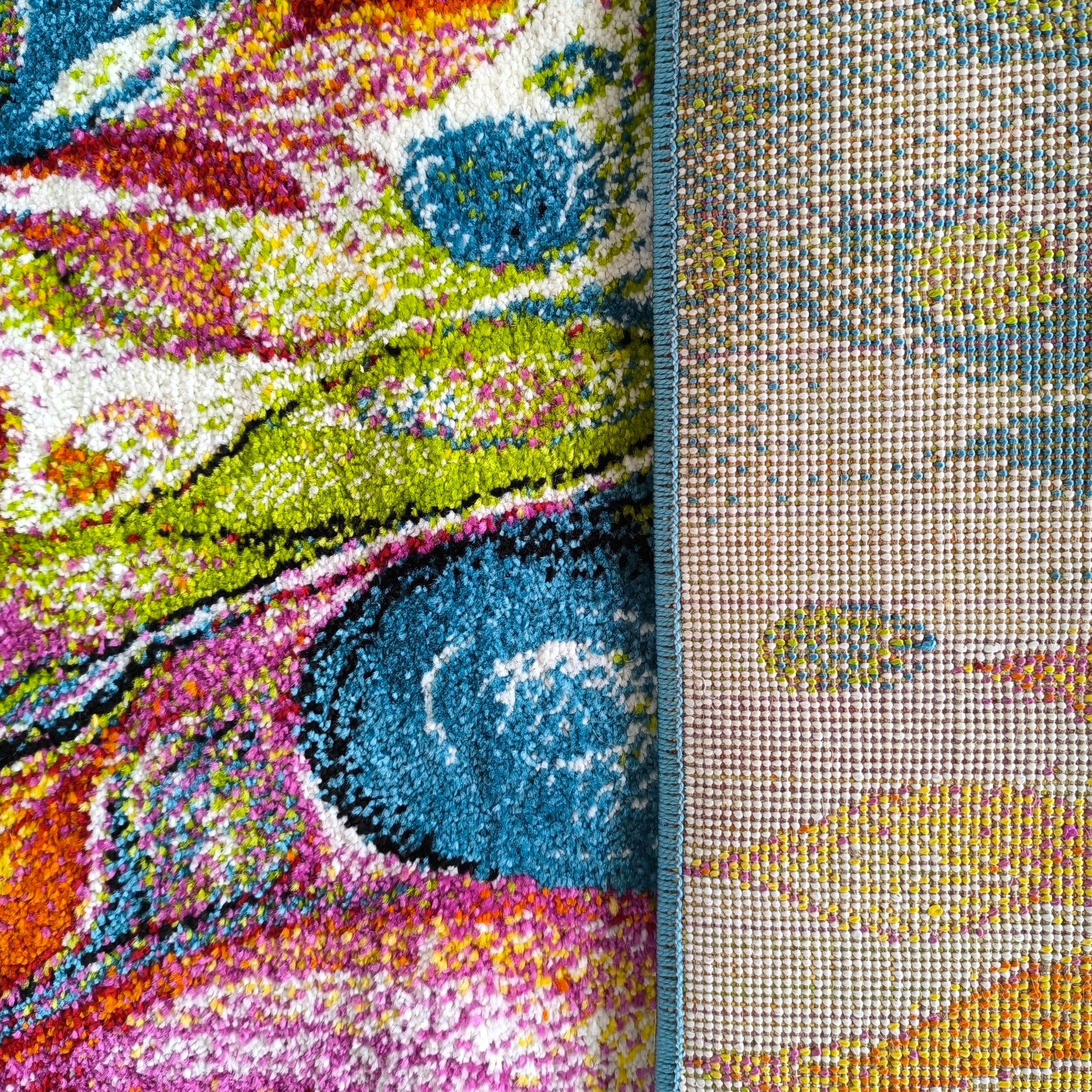 Tapis à poils longs aux motifs abstraits vifs : turquoise, vert, rose, orange. Une bordure bleue sépare le côté tissé apparent et coloré