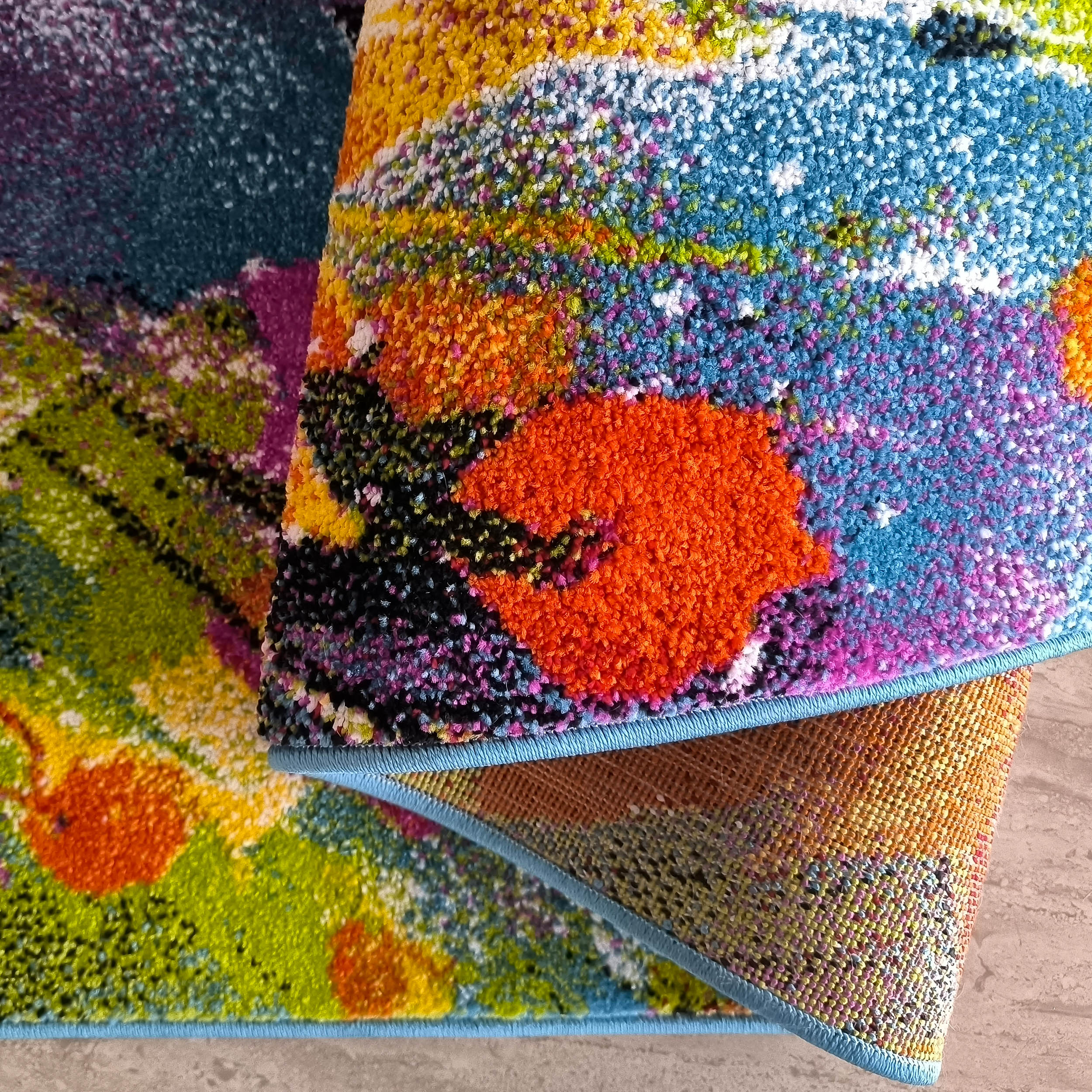 Tapis à motifs floraux abstraits et texture épaisse aux couleurs vives: orange, vert, bleu, jaune, magenta. Ourlet bleu clair visible