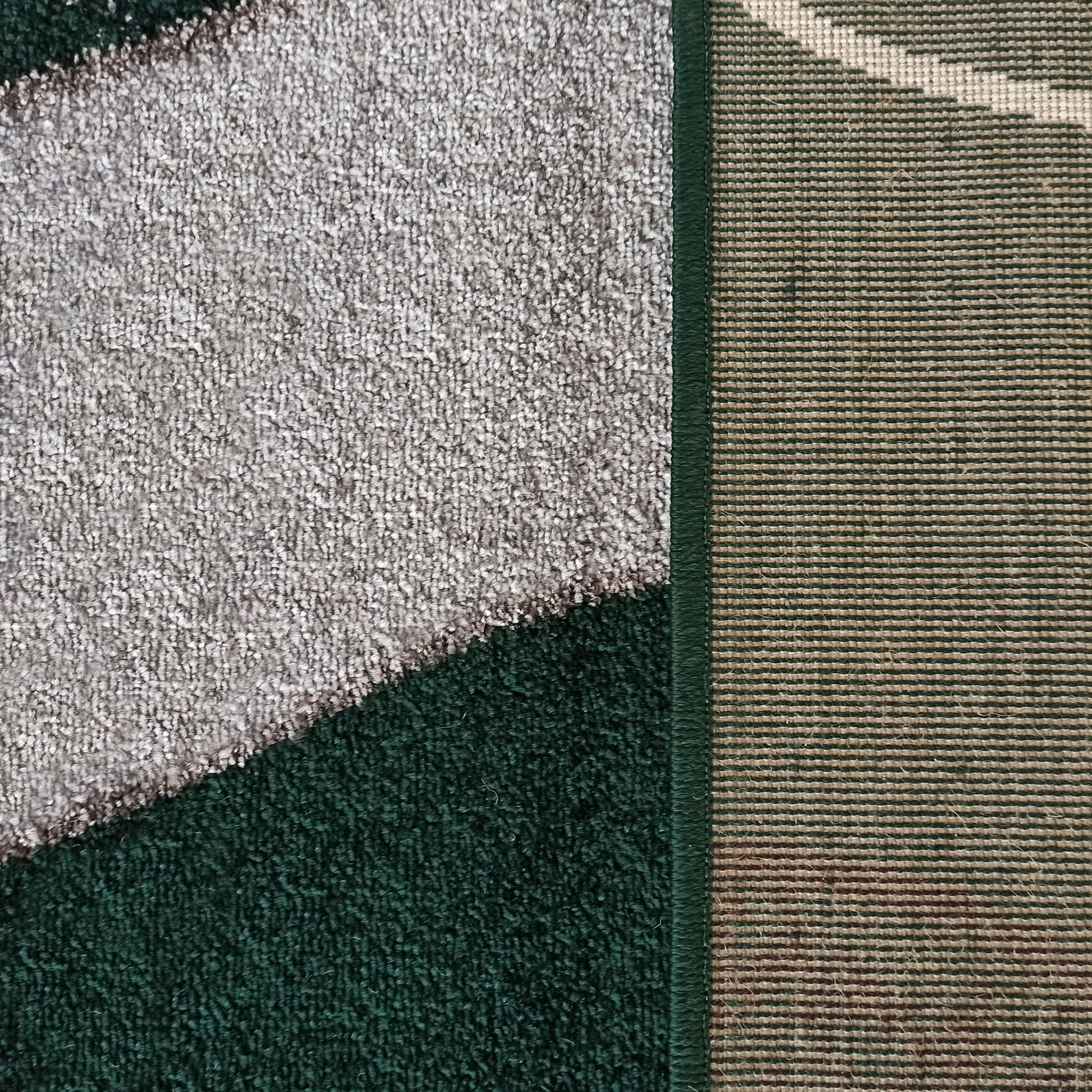 Tapis à poils courts avec motifs géométriques gris clair et vert foncé. L'envers tissé à rayures beiges et vertes est visible sur le côté