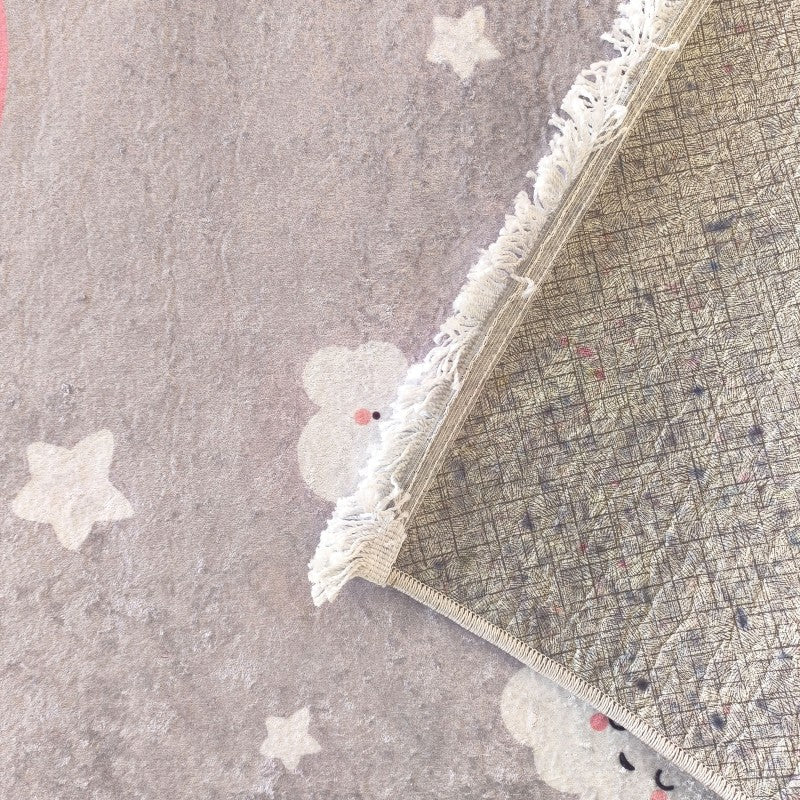 Tapis gris clair à texture moelleuse, orné d'étoiles et de nuages blancs avec des touches de rose, plié montrant son envers quadrillé et ses franges blanches