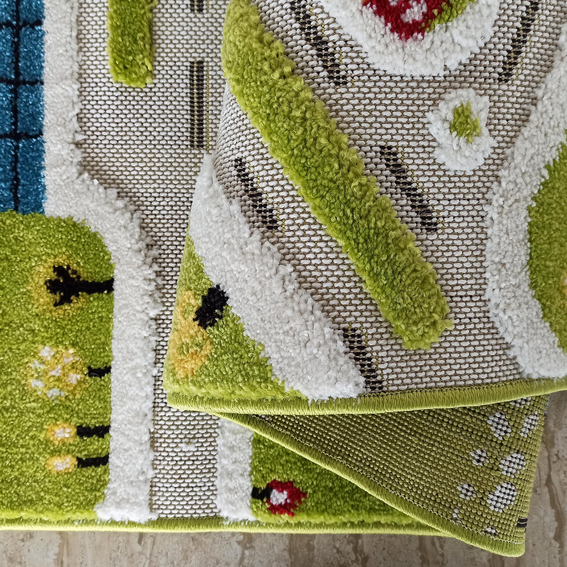 Tapis enfant à motifs de routes, arbres et maisons en vert, blanc, bleu, rouge, jaune et noir. Texture bouclée et tissée