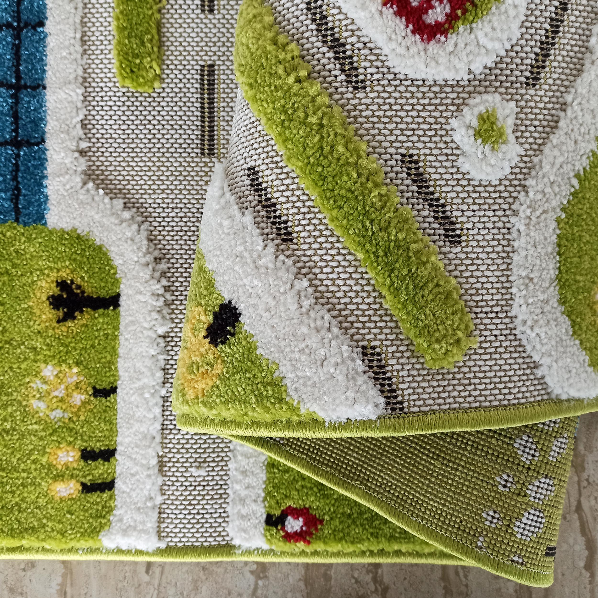 Tapis enfant à motifs de routes, arbres et maisons en vert, blanc, bleu, rouge, jaune et noir. Texture bouclée et tissée