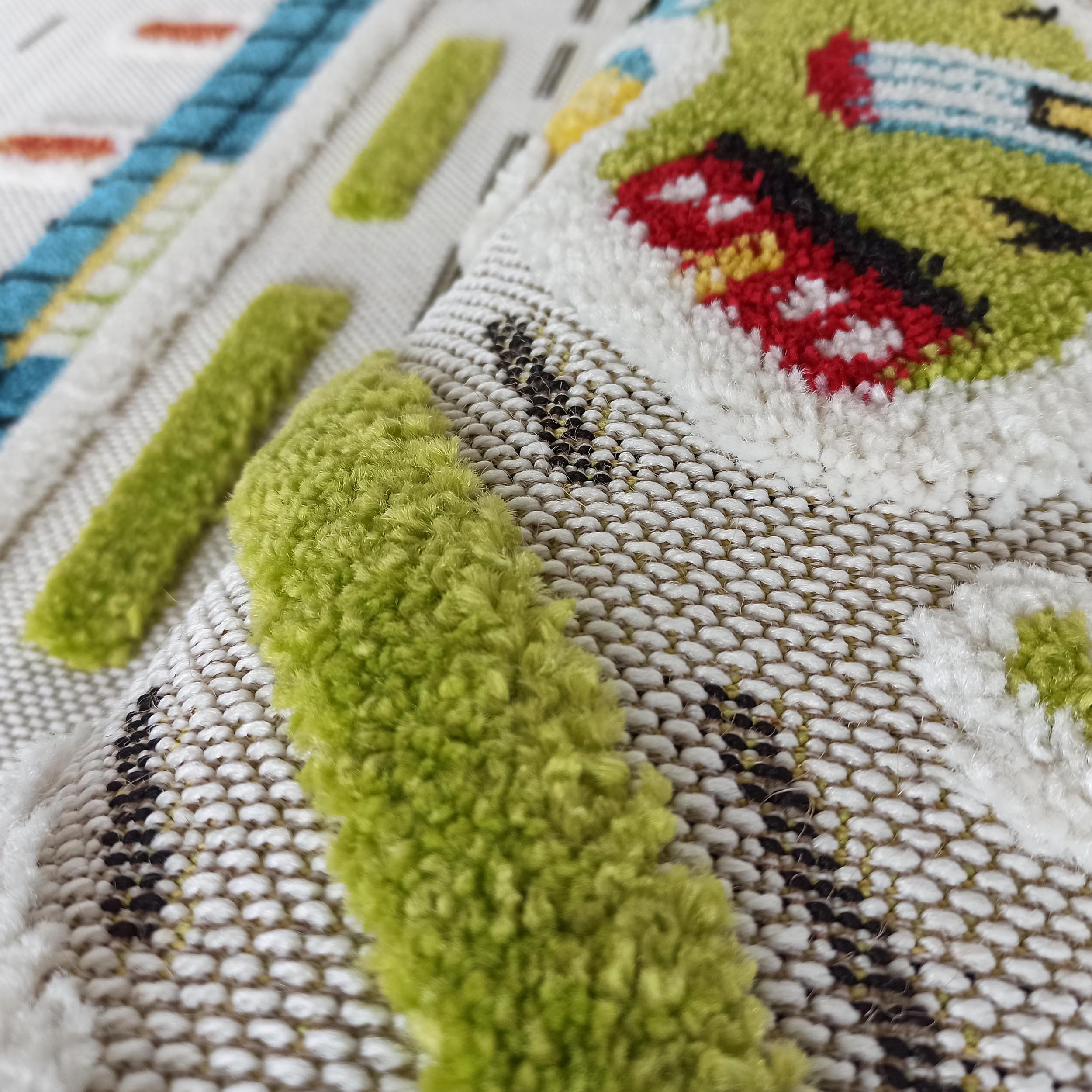 Tapis coloré aux motifs ludiques en relief verts, rouges et bleus sur un fond tissé blanc et noir, avec différentes textures