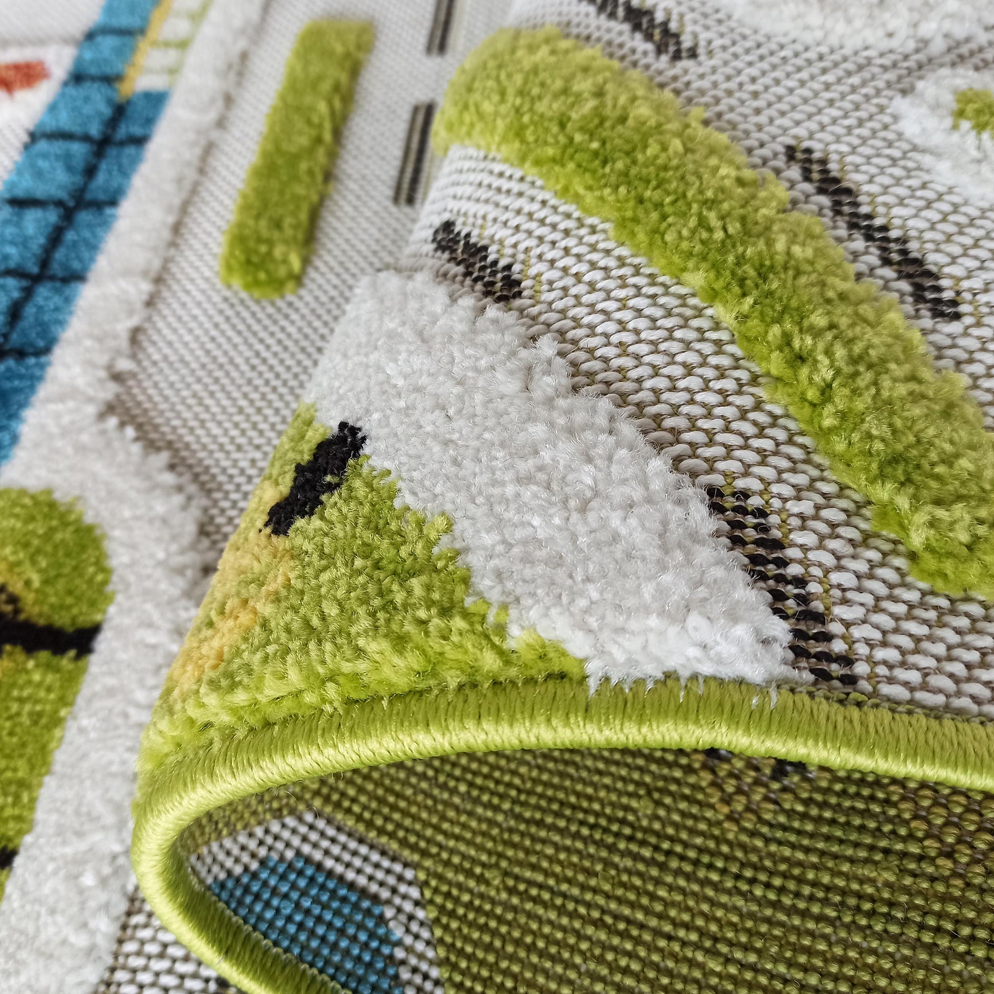 Gros plan sur un tapis aux motifs géométriques verts, blancs et noirs, avec des accents bleus, présentant des textures de poils et de tissage plat