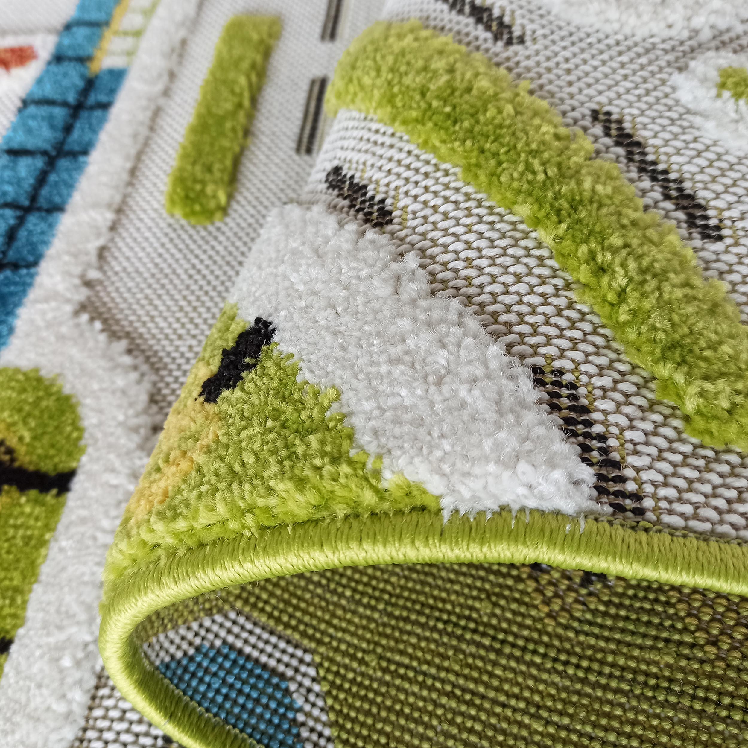 Gros plan sur un tapis aux motifs géométriques verts, blancs et noirs, avec des accents bleus, présentant des textures de poils et de tissage plat
