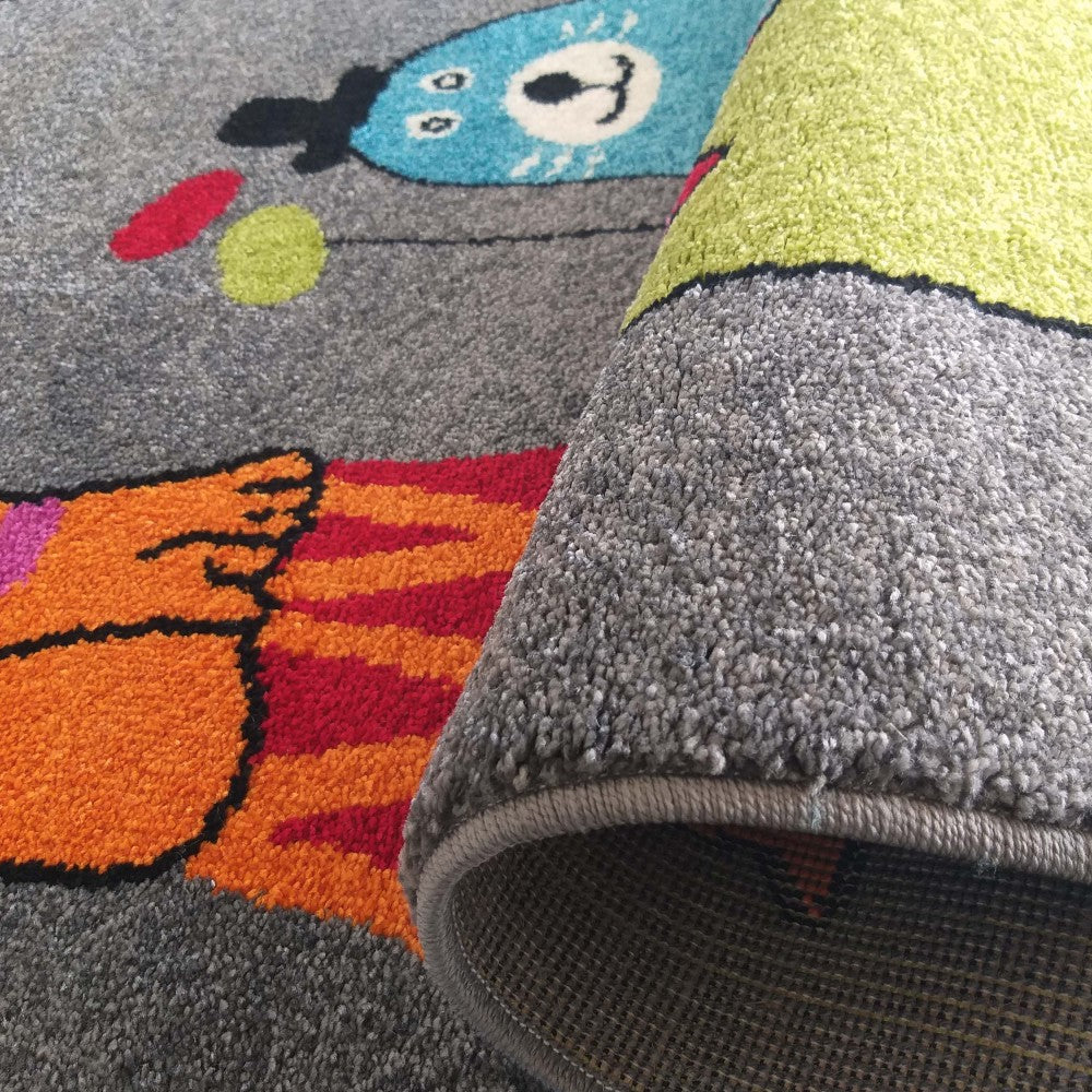 Tapis doux à motifs colorés figuratifs bleus, orange et verts sur un fond gris chiné, avec un bord roulé
