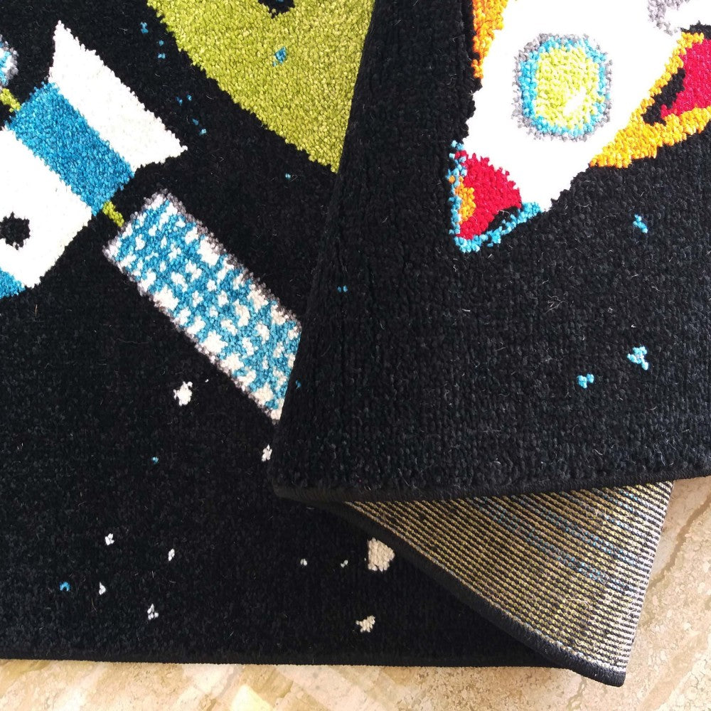 Tapis noir à motifs spatiaux colorés (blanc, bleu, vert, jaune, rouge). Une partie est pliée, révélant son envers tissé clair