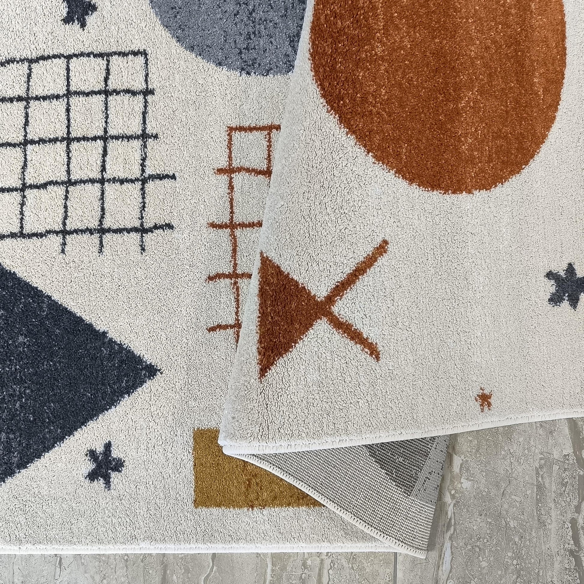 Tapis crème à motifs géométriques variés gris anthracite, rouille et jaune moutarde, avec une partie enroulée
