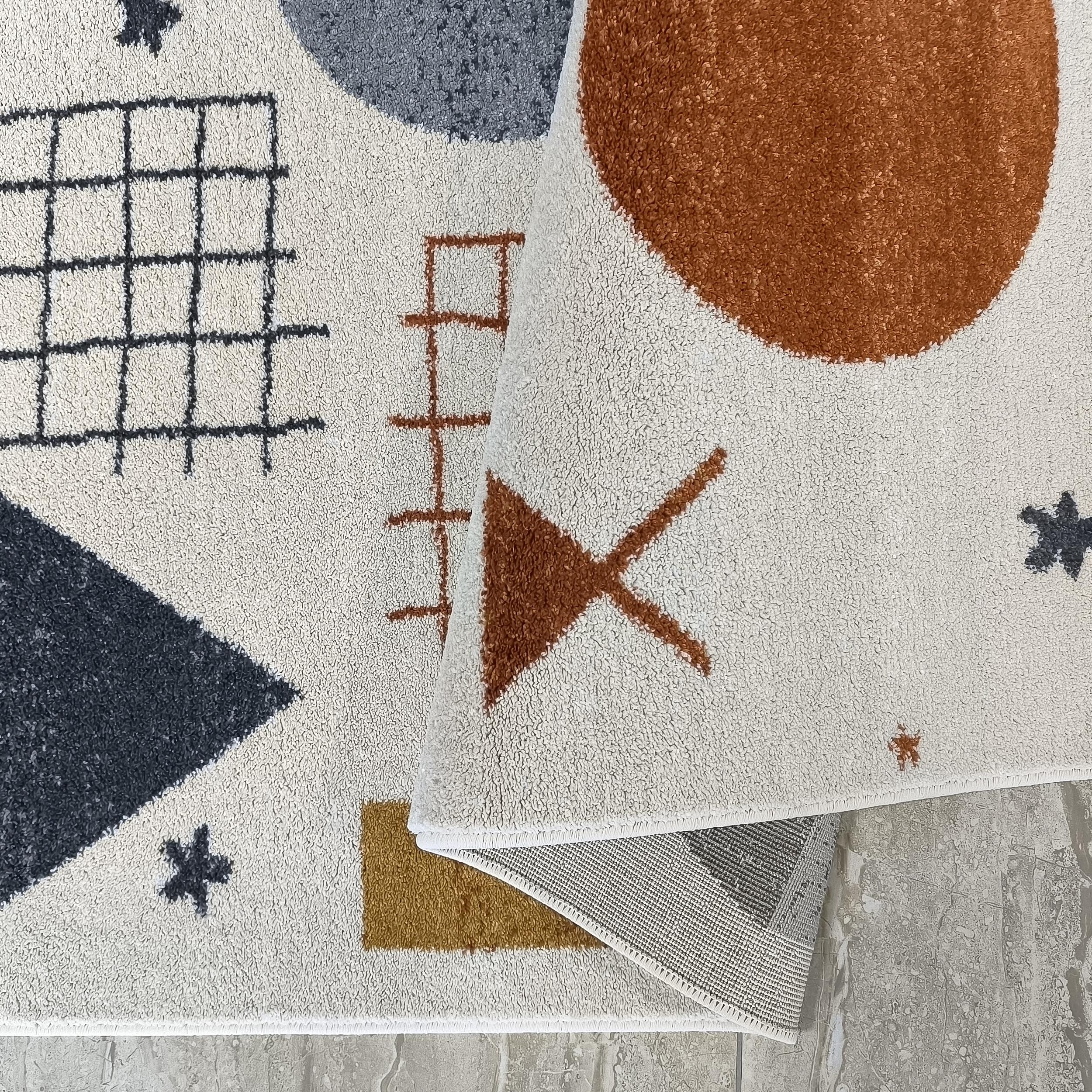 Tapis crème à motifs géométriques variés gris anthracite, rouille et jaune moutarde, avec une partie enroulée
