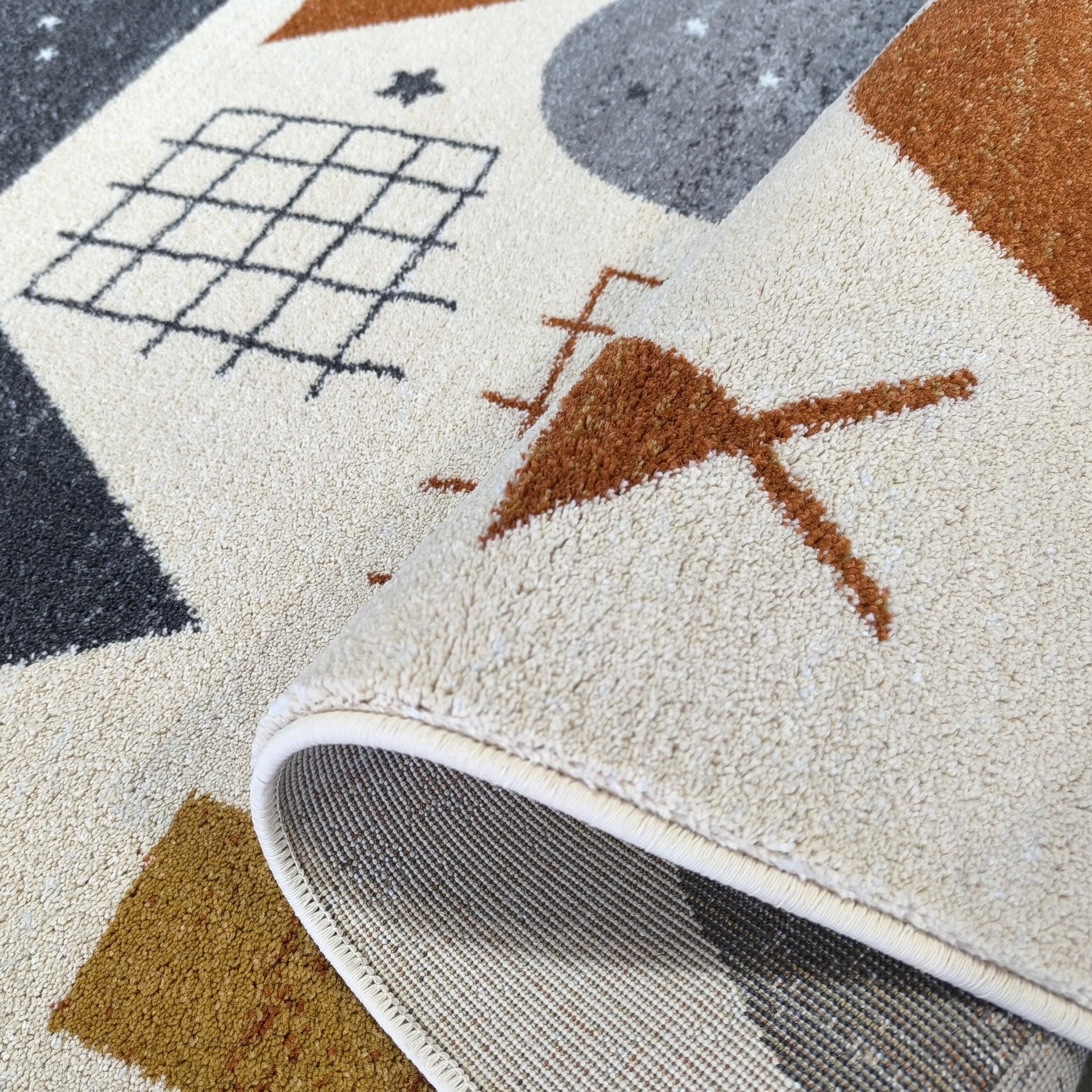 Tapis aux motifs géométriques beiges, gris foncé, terre de Sienne et ocre. Sa texture douce est visible, avec une partie enroulée montrant son envers tissé