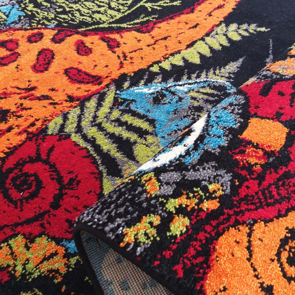 Tapis coloré à poils courts, présentant des motifs abstraits et floraux en rouge, orange, bleu et vert sur fond noir, partiellement roulé