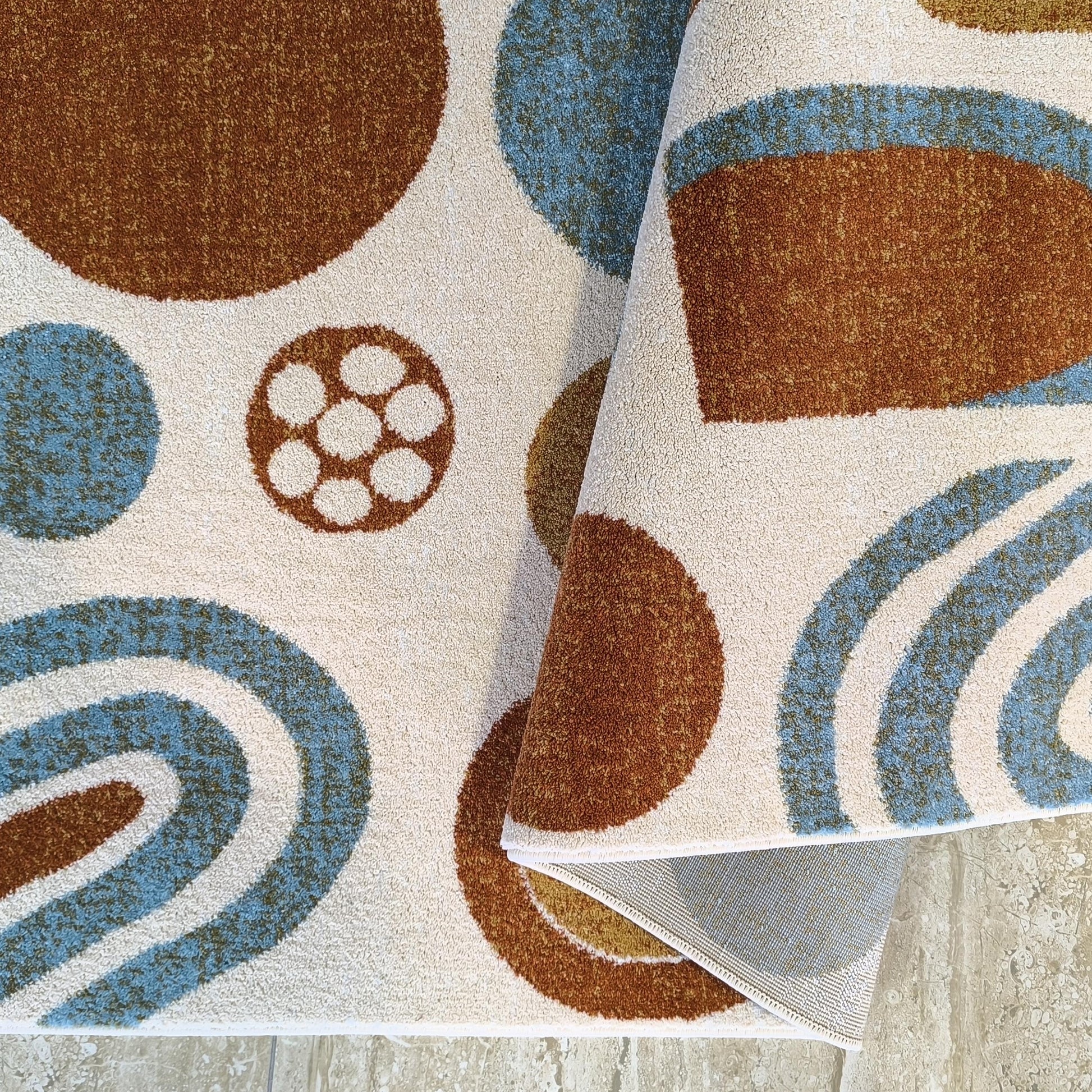 Tapis crème à poils courts avec motifs de cercles et d'arcs marron et bleu clair, enroulé sur un carrelage clair