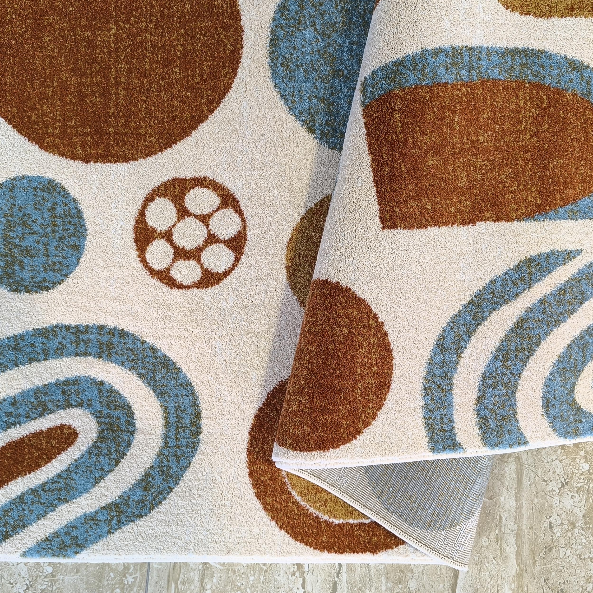 Tapis crème à poils courts avec motifs de cercles et d'arcs marron et bleu clair, enroulé sur un carrelage clair