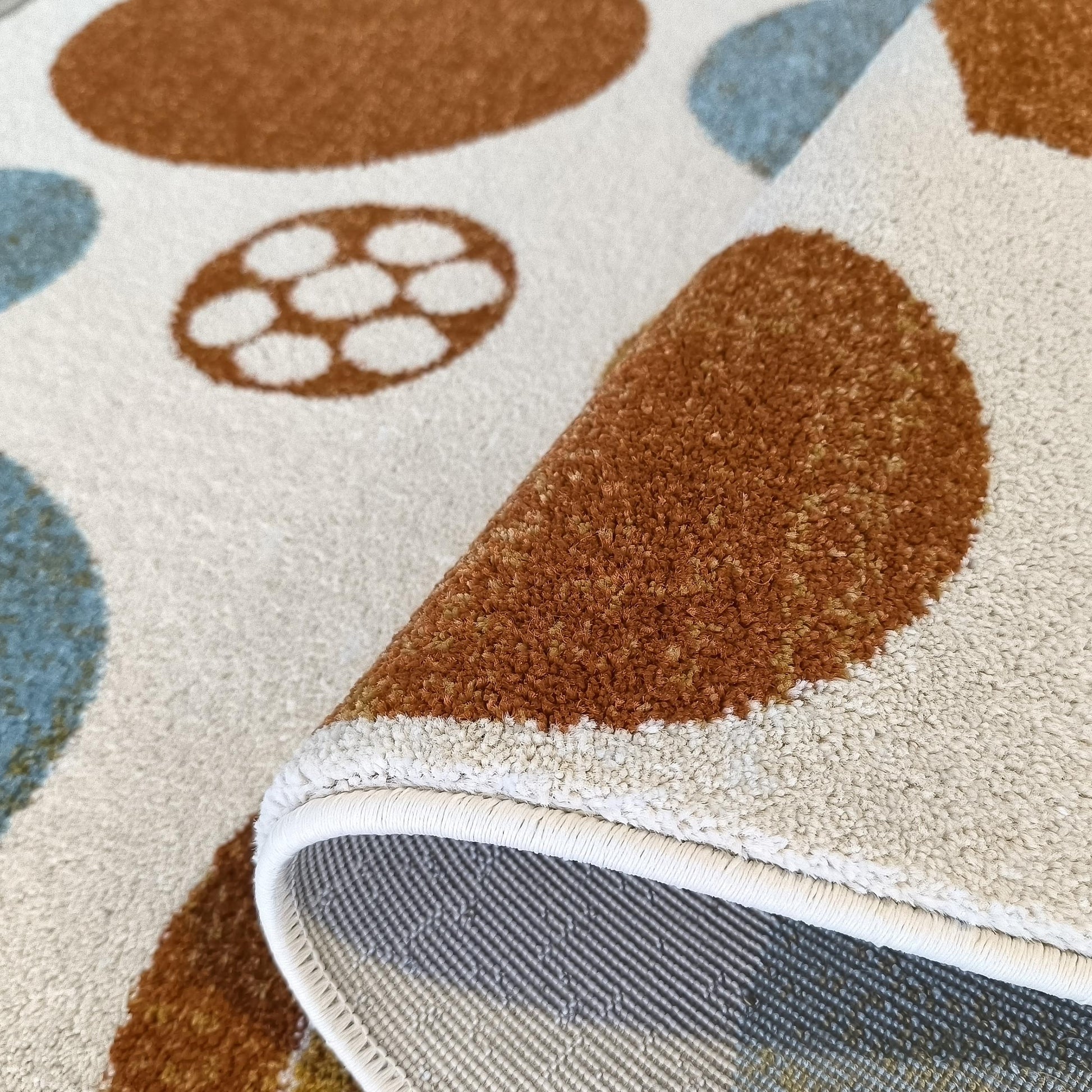 Tapis moelleux aux motifs ronds et abstraits marron et bleus sur fond crème, un coin relevé révélant l'envers