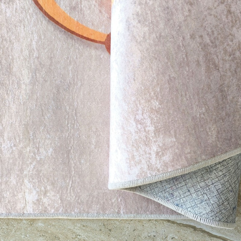 Tapis doux beige clair avec un motif orangé, partiellement roulé pour montrer son envers gris quadrillé et sa bordure